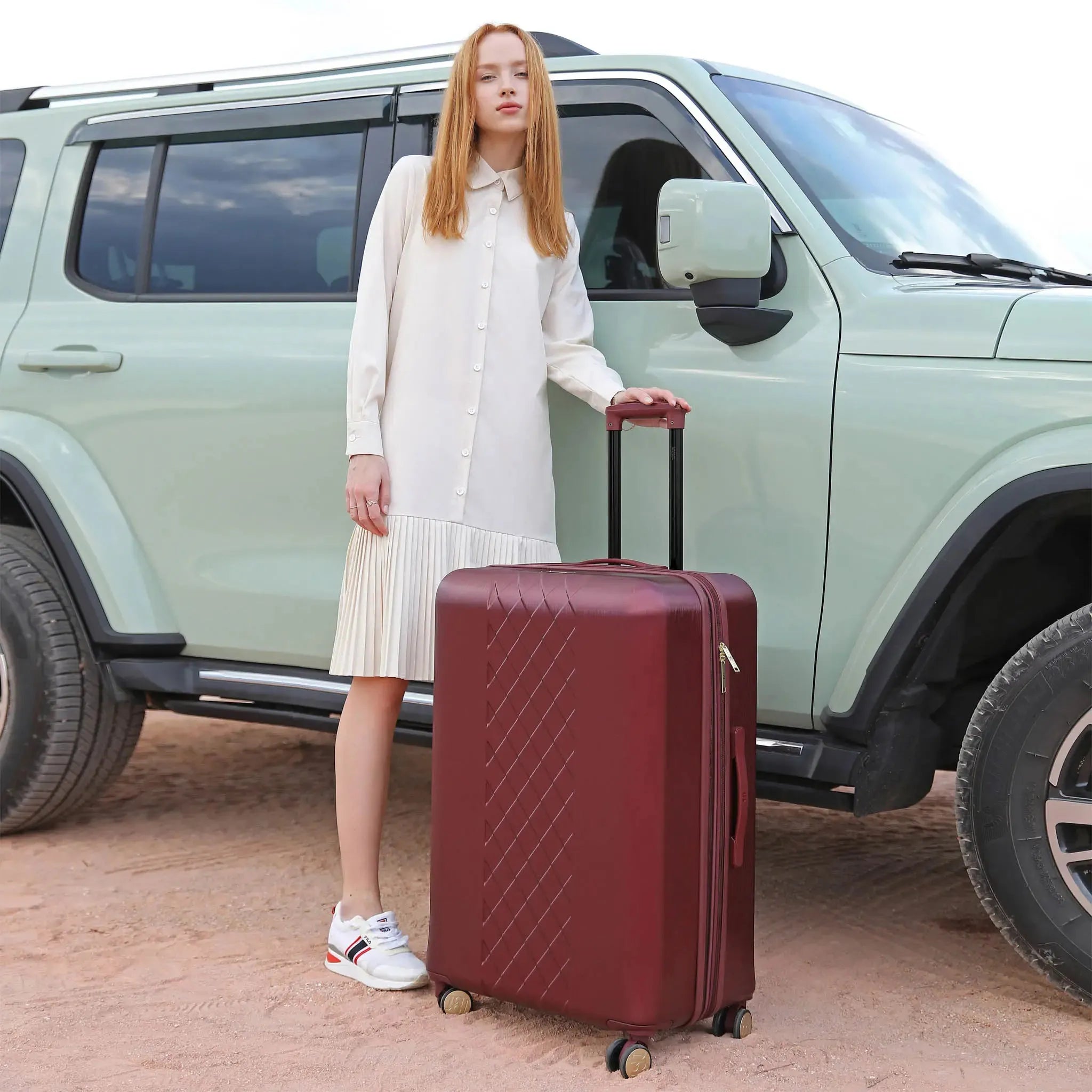 Woman with a red suitcase standing next to a light green SUV on a dirt road.