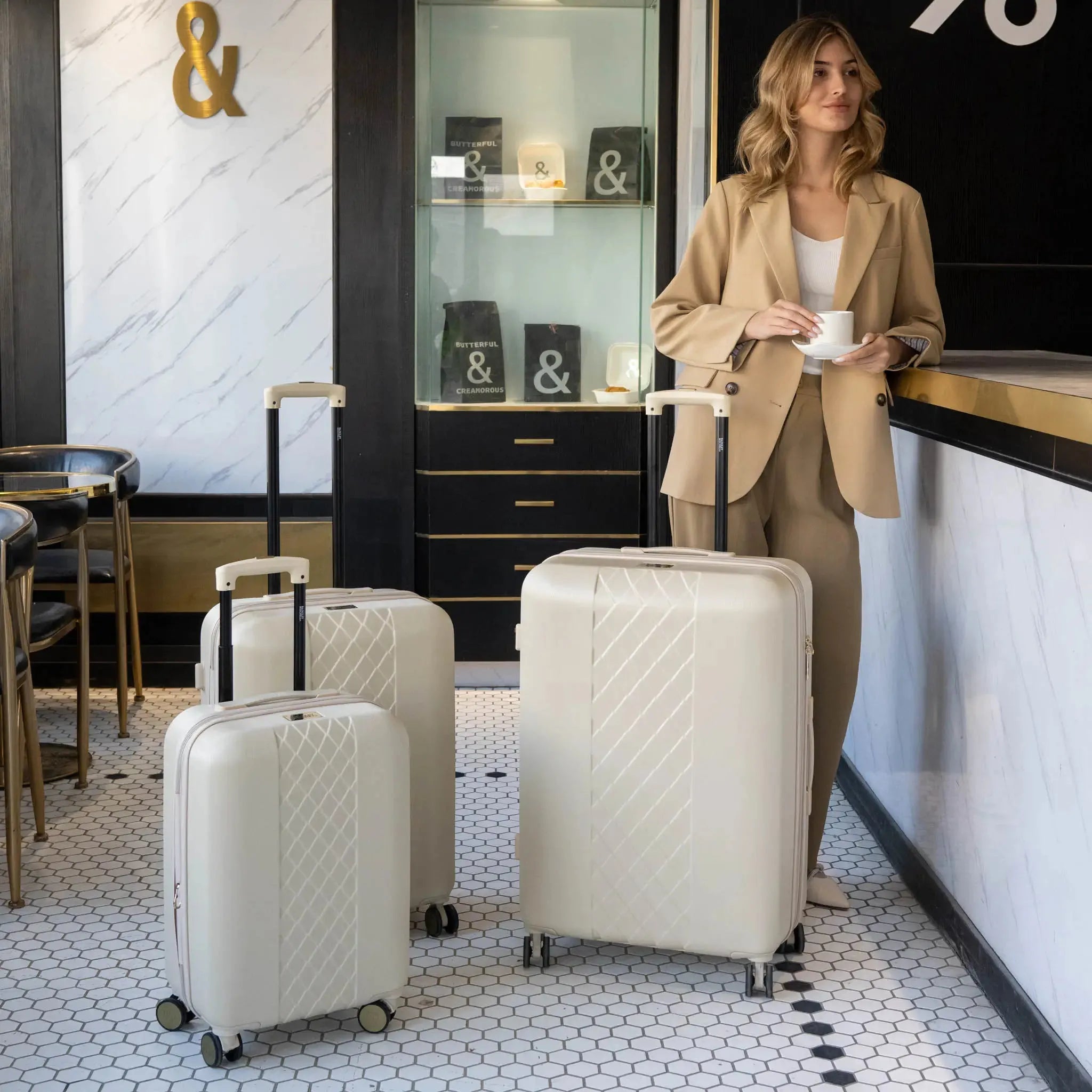 Woman in a beige suit standing next to white suitcases in a stylish interior setting.