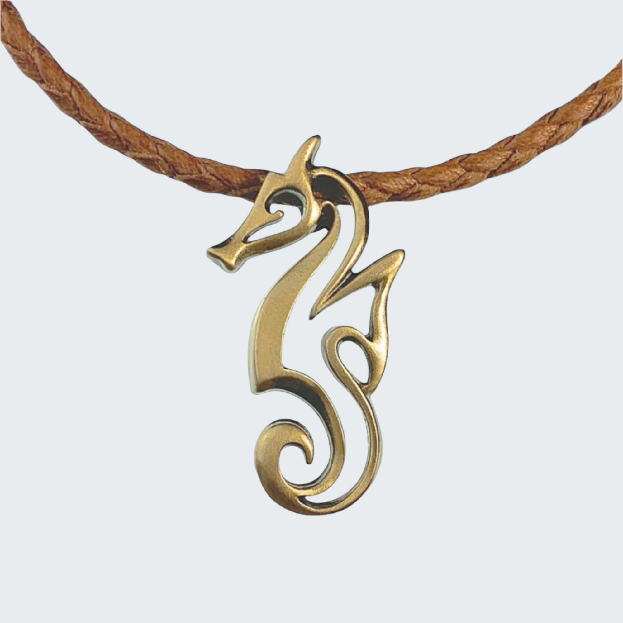 Gold seahorse pendant on a brown cord with a beach background