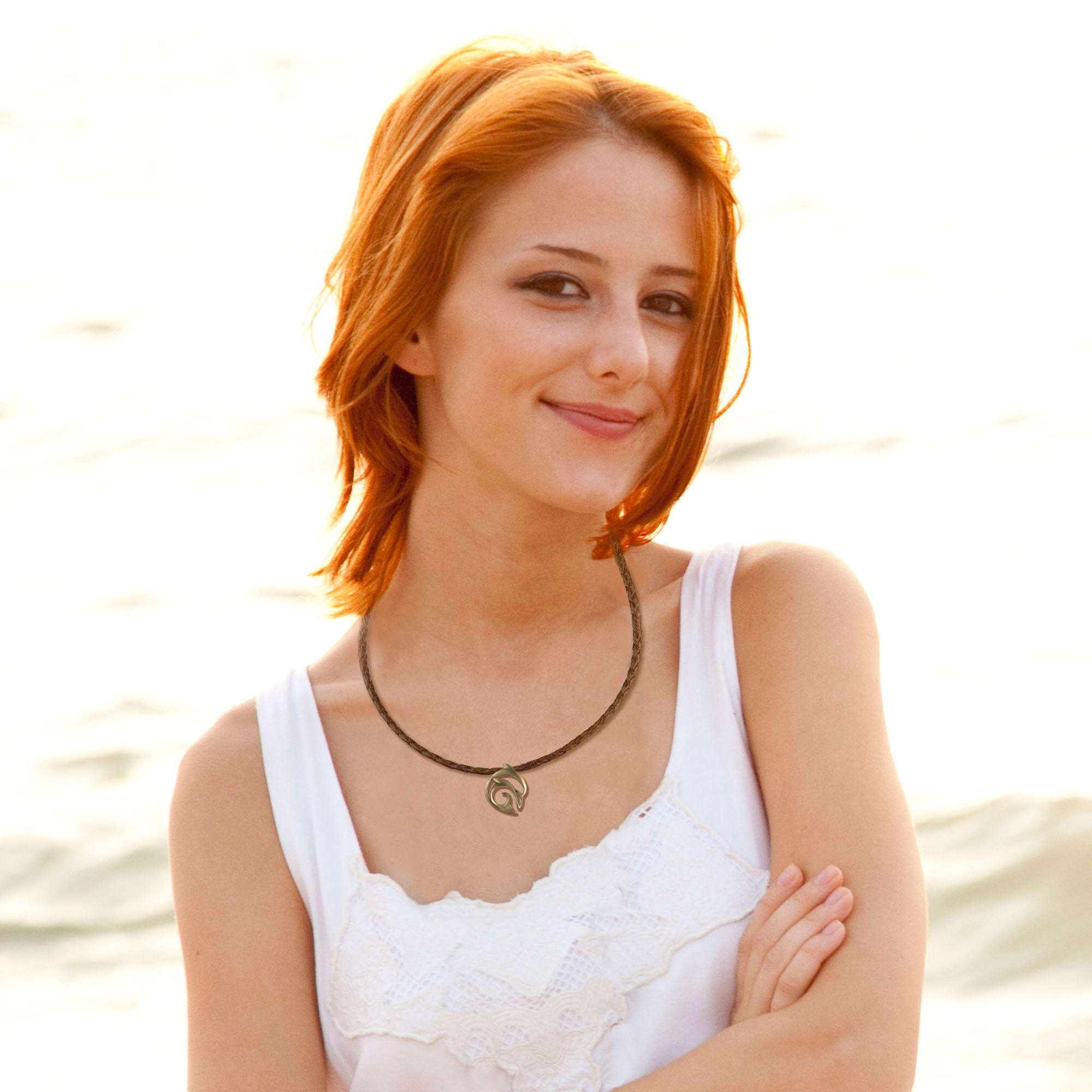 Woman with red hair wearing a white top and necklace by a body of water.