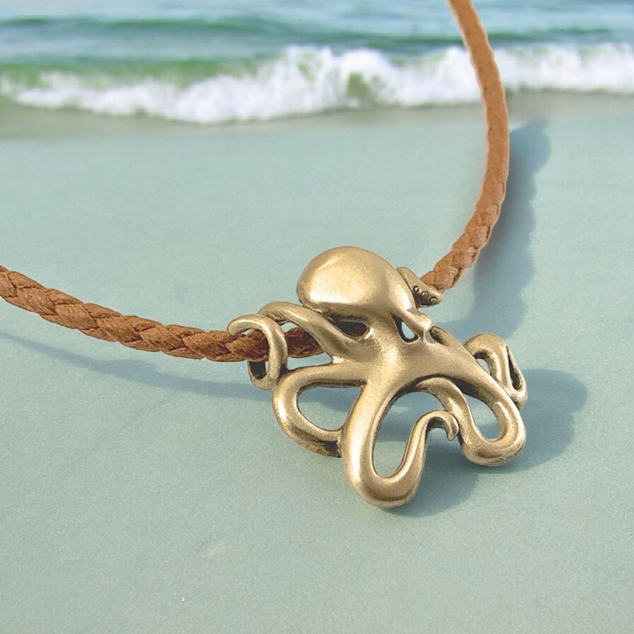 Brass octopus pendant on a brown cord with a beach background