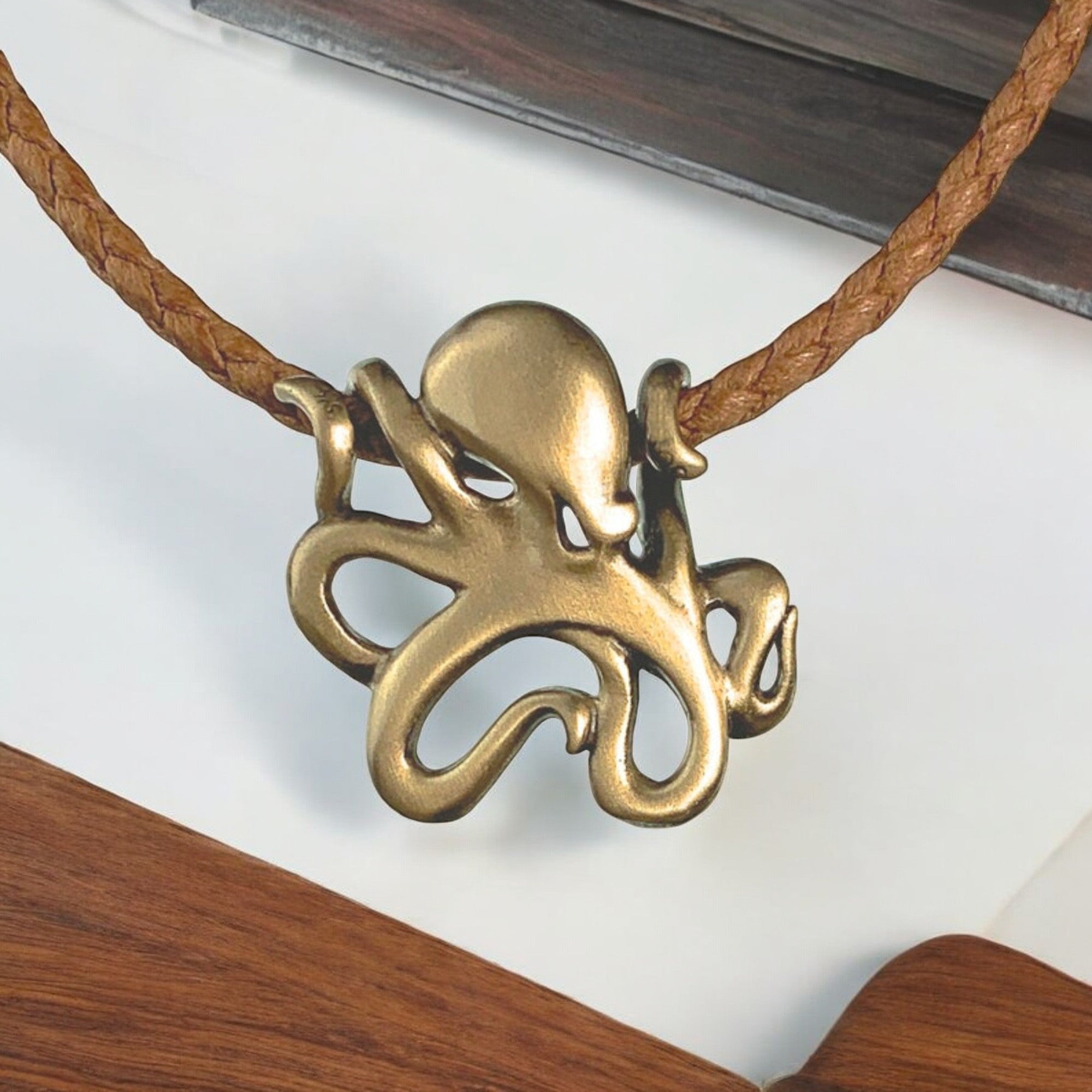 Brass octopus pendant on a brown cord with a wooden surface and white paper background
