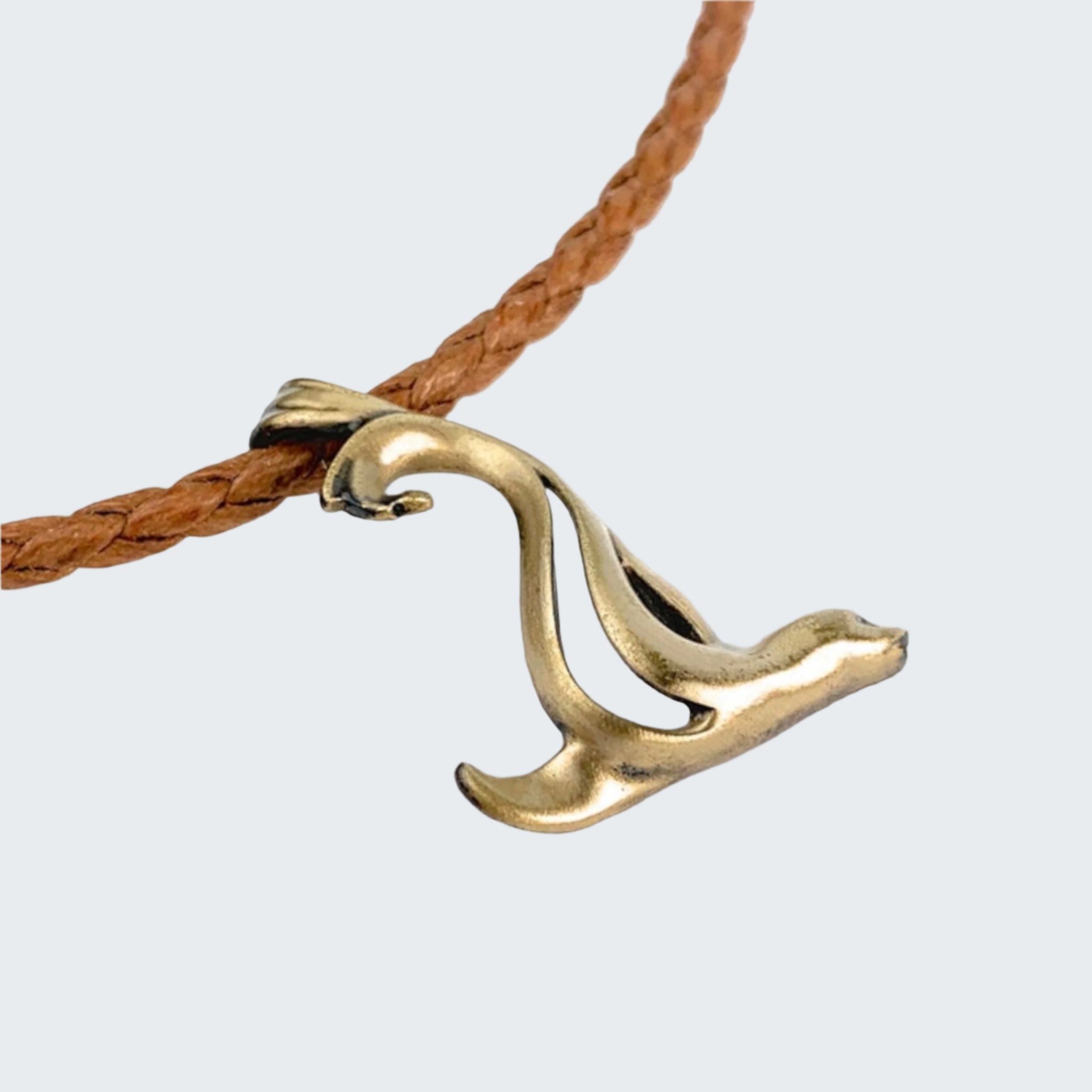 Gold wave-shaped pendant on a brown cord against a light gray background