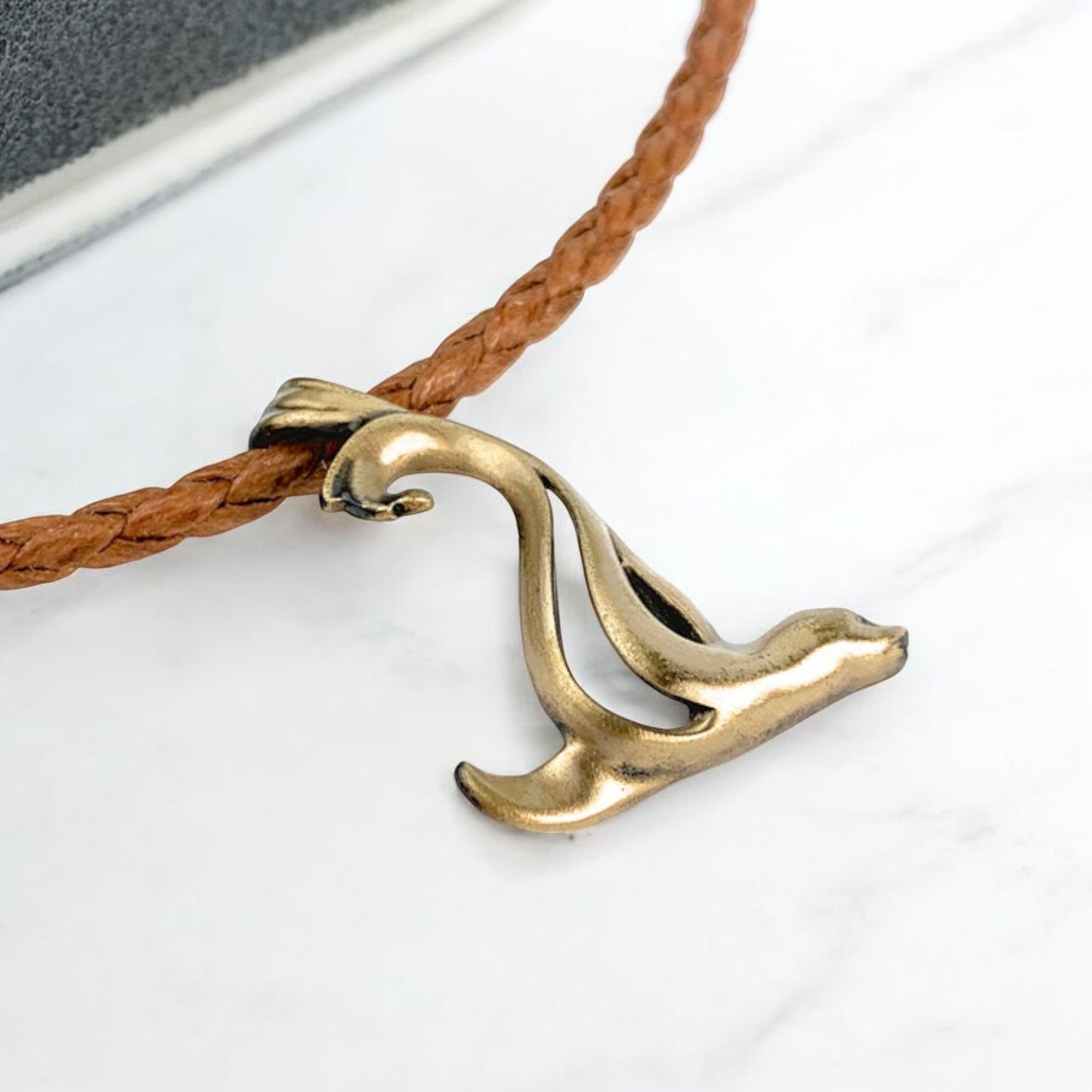Brass wave-shaped pendant on a brown cord against a white background
