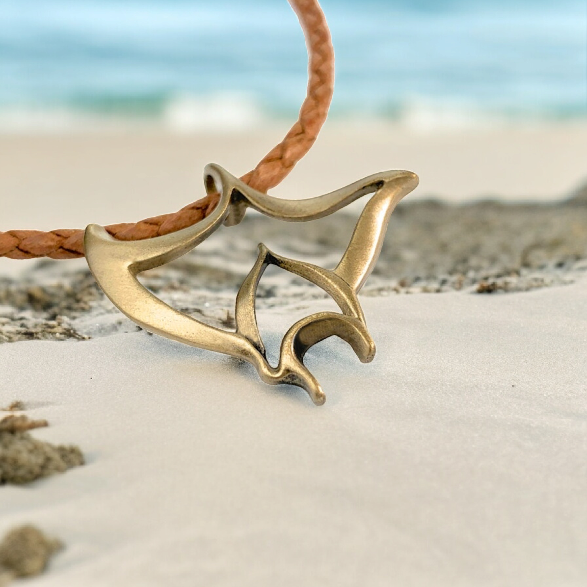 Brass fish-shaped pendant on a leather cord against a beach background