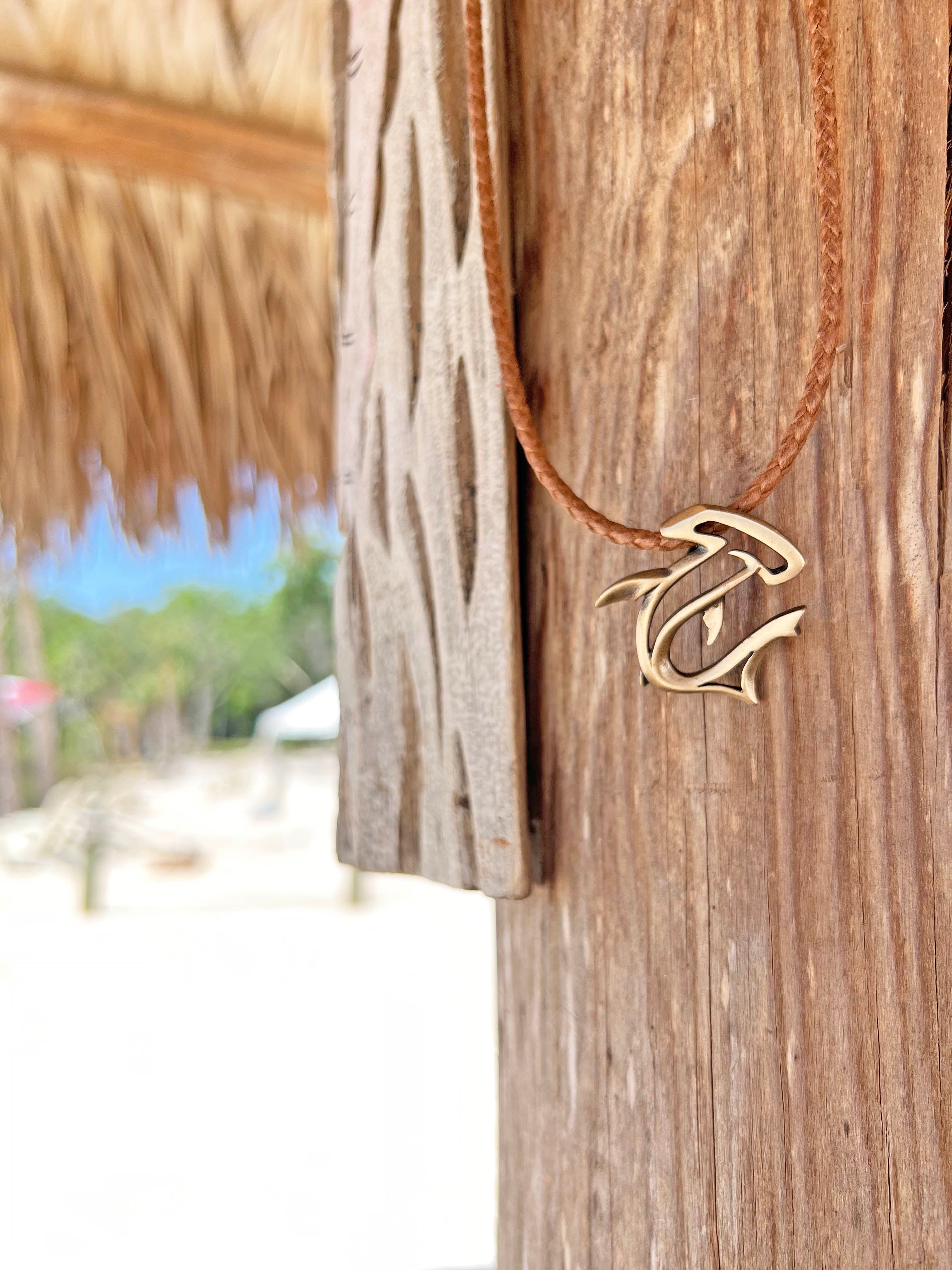Gold necklace with a leaf-shaped pendant hanging on a wooden post with a blurred beach background.