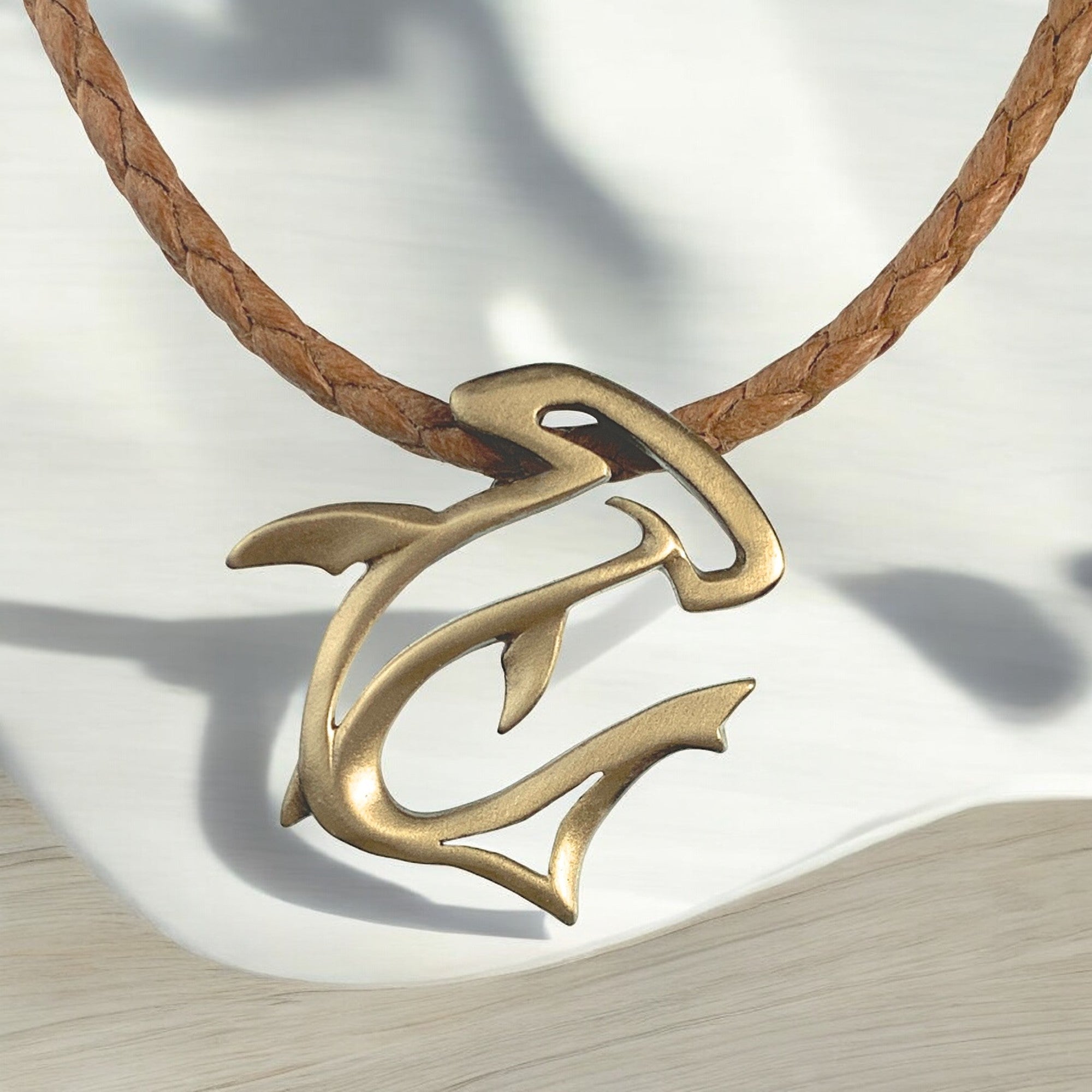 Brass anchor-shaped pendant on a brown leather cord against a light background