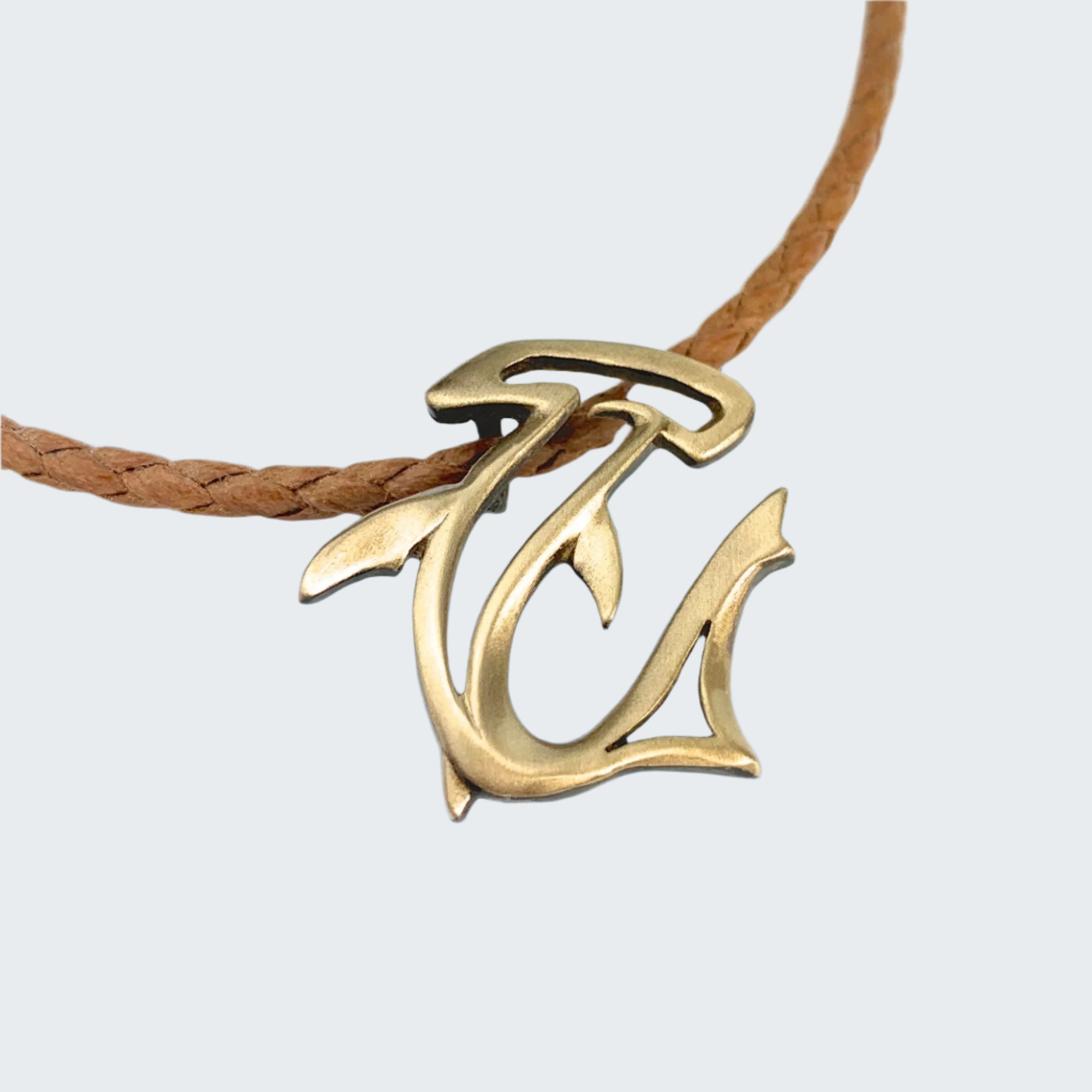 Gold fish hook pendant on a leather cord with water in the background