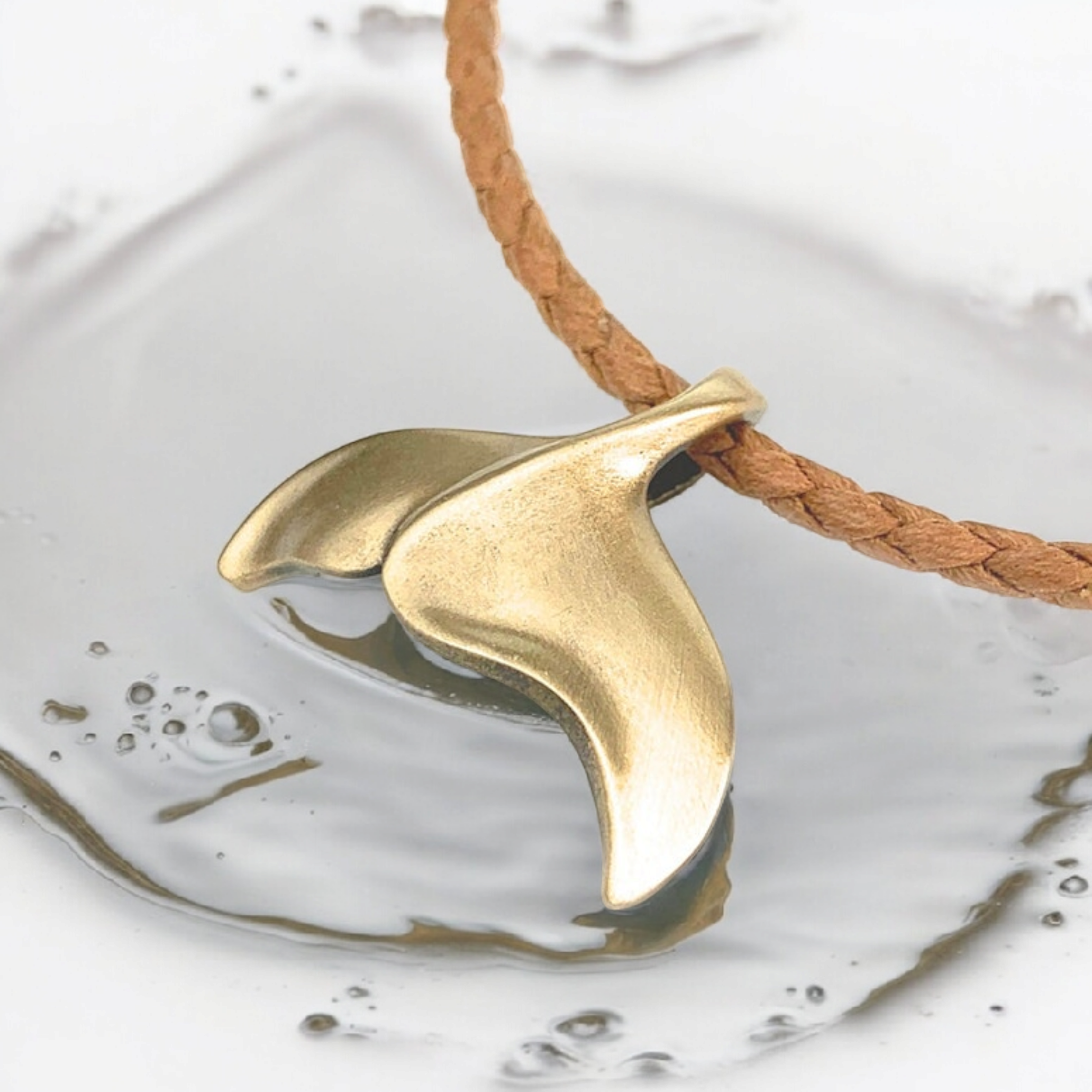 Gold fish-shaped pendant on a braided cord over water