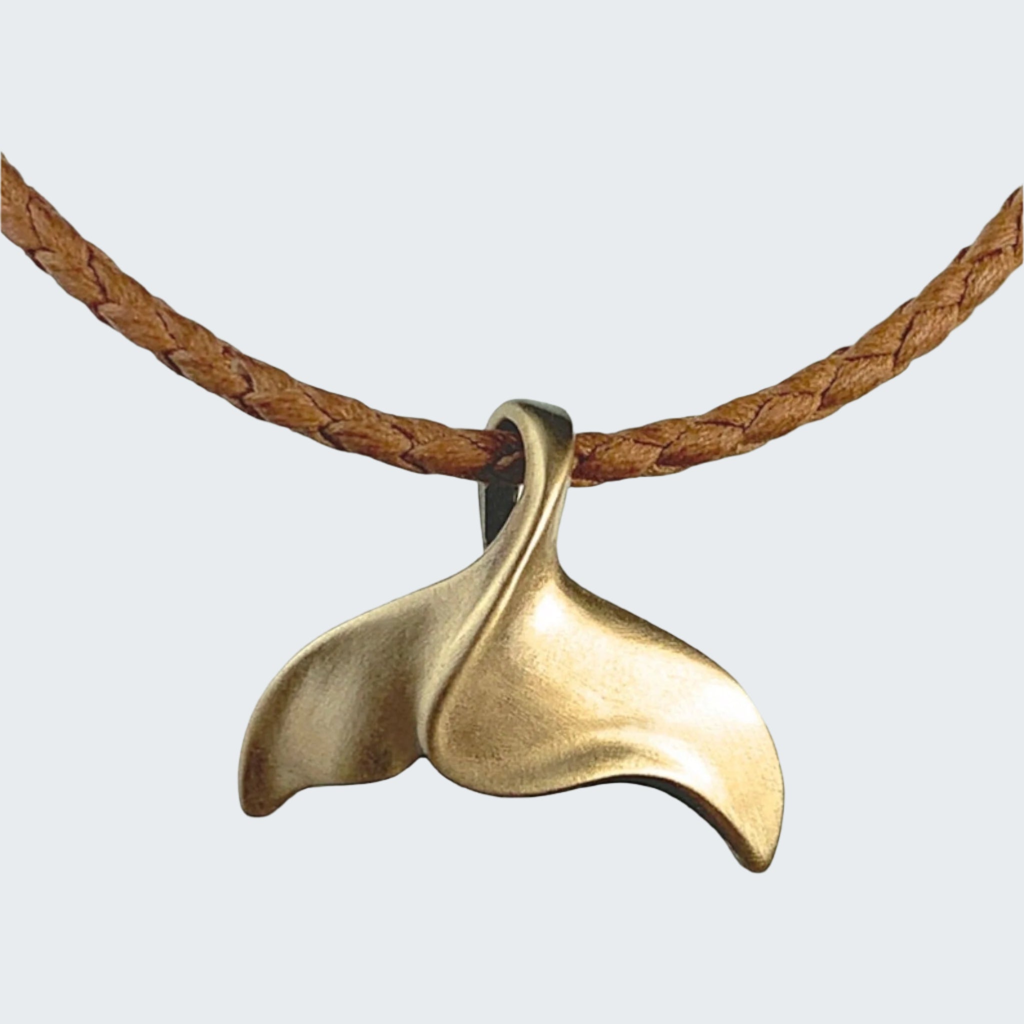 Bronze whale tail pendant on a leather cord with a beach background