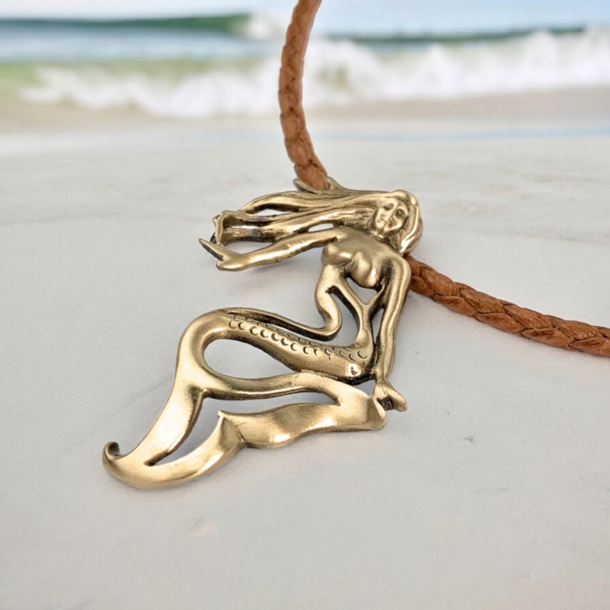Bronze mermaid pendant on a leather cord against a beach background