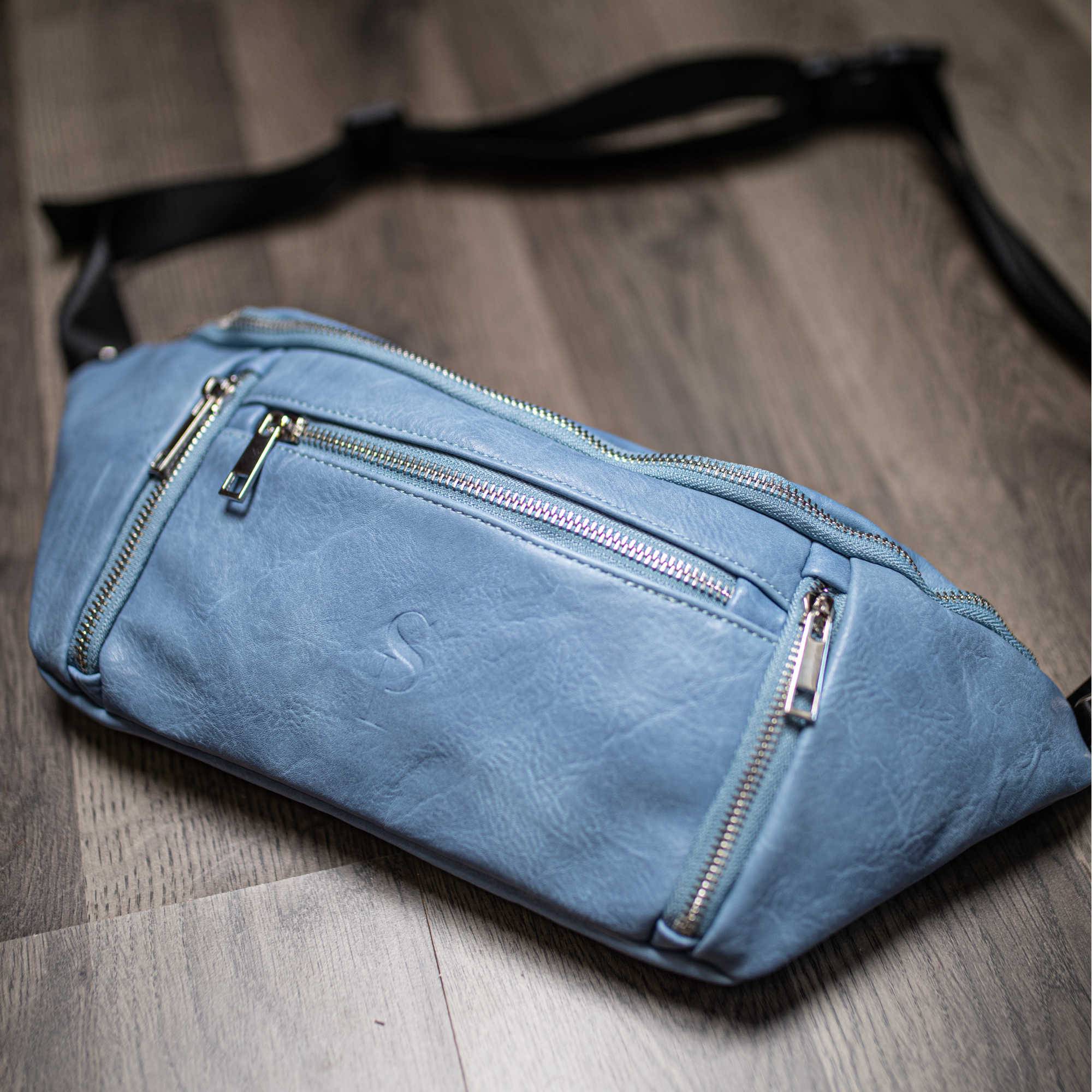 Blue waist bag with zippers on a wooden floor