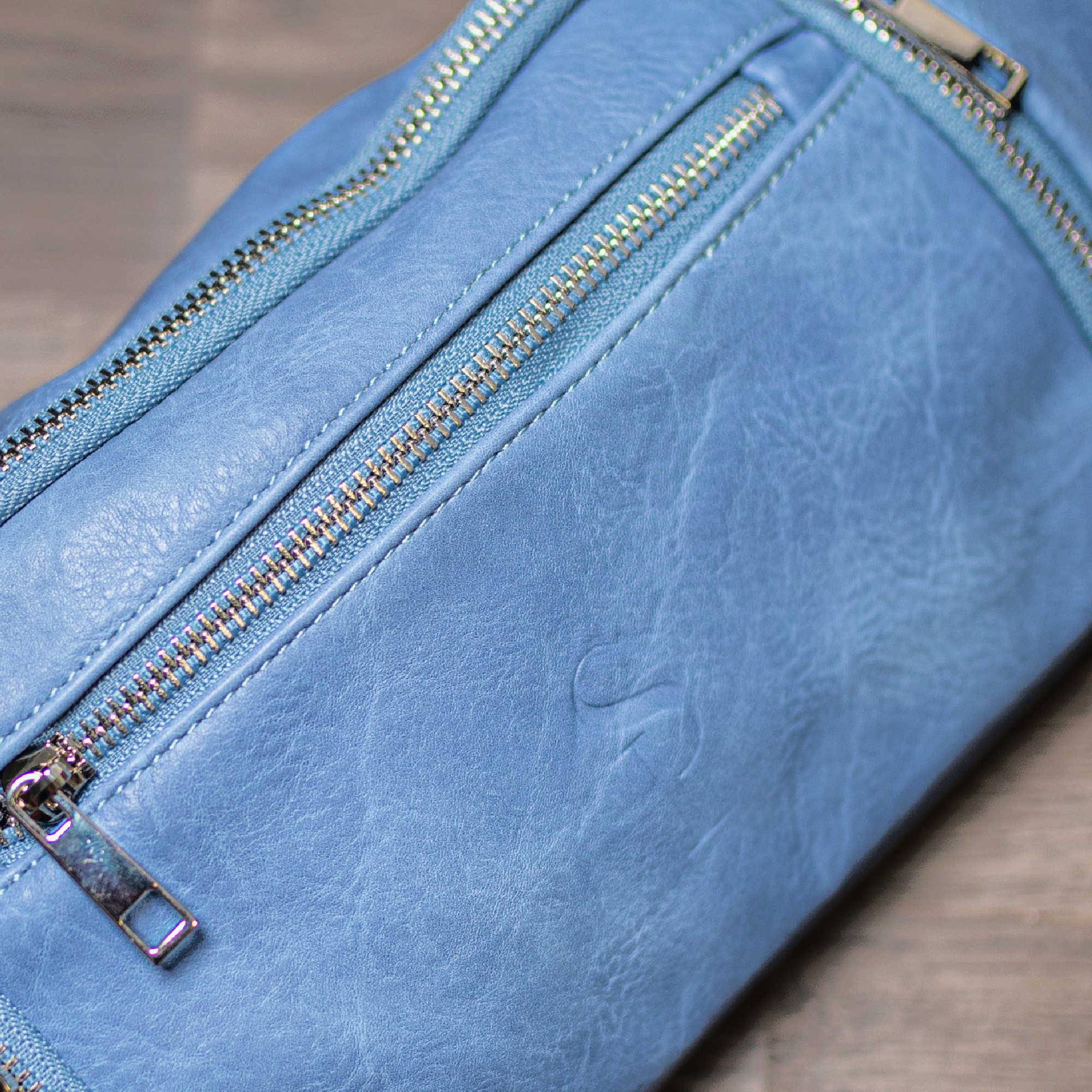 Close-up of a blue leather pouch with zippers on a wooden surface