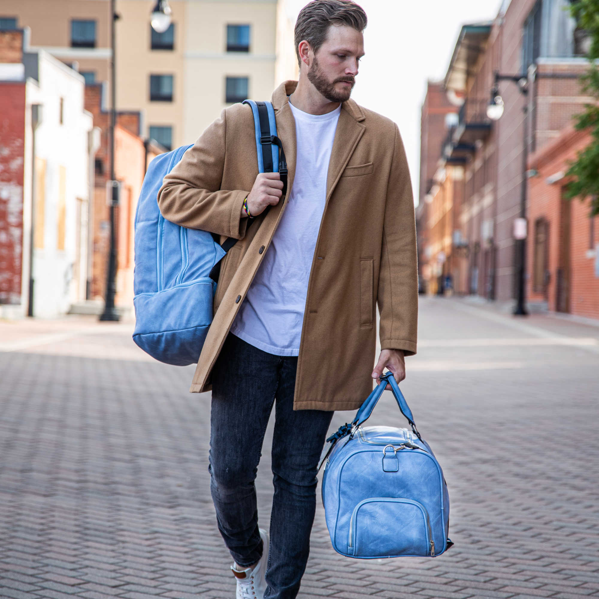 Man walking on a street holding two blue bags