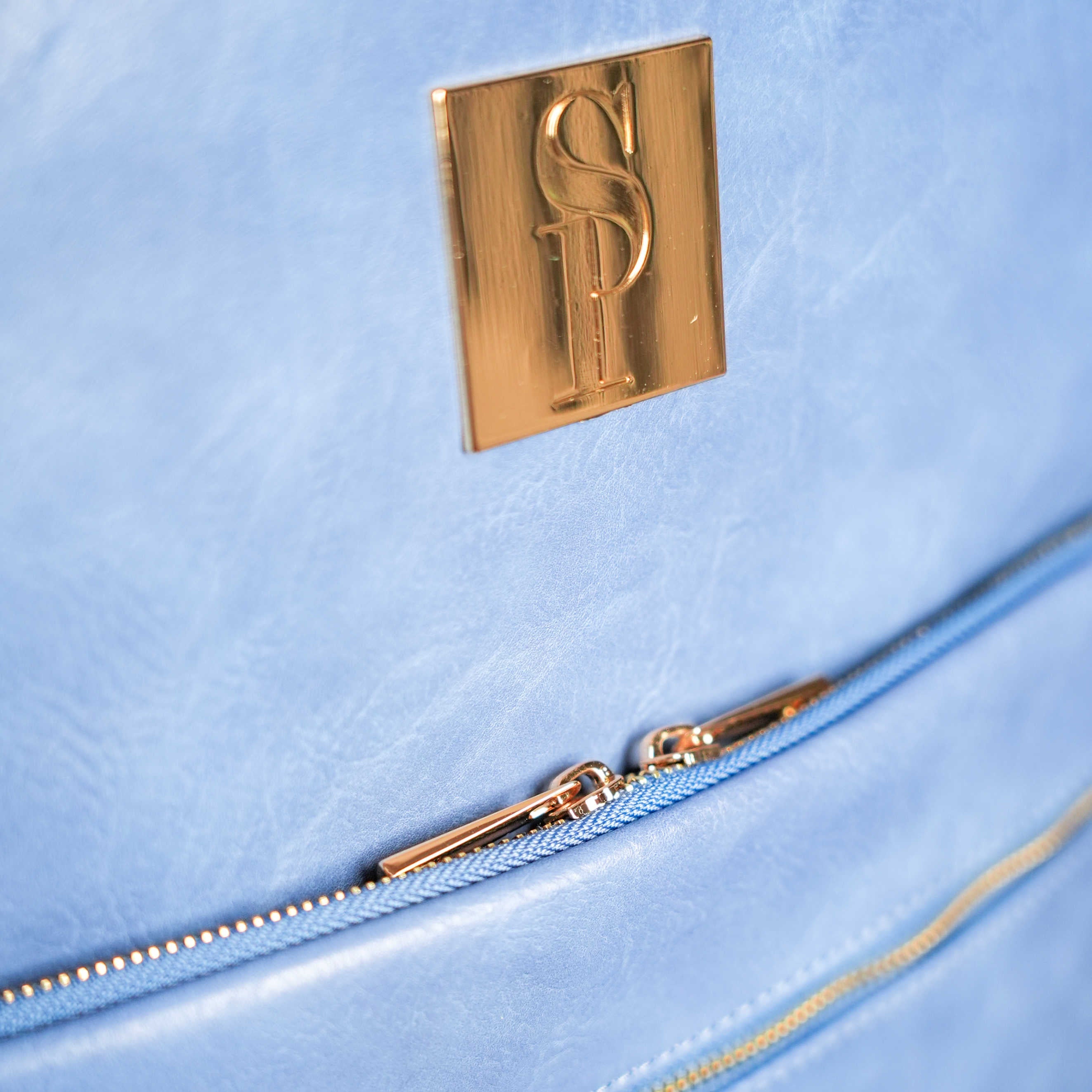 Close-up of a light blue bag with a gold zipper and logo.