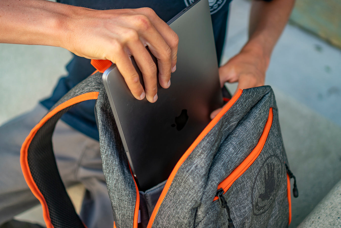 Person placing a laptop into a gray backpack with orange accents.