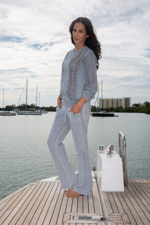 Woman in light gray outfit standing on a dock with water and boats in the background