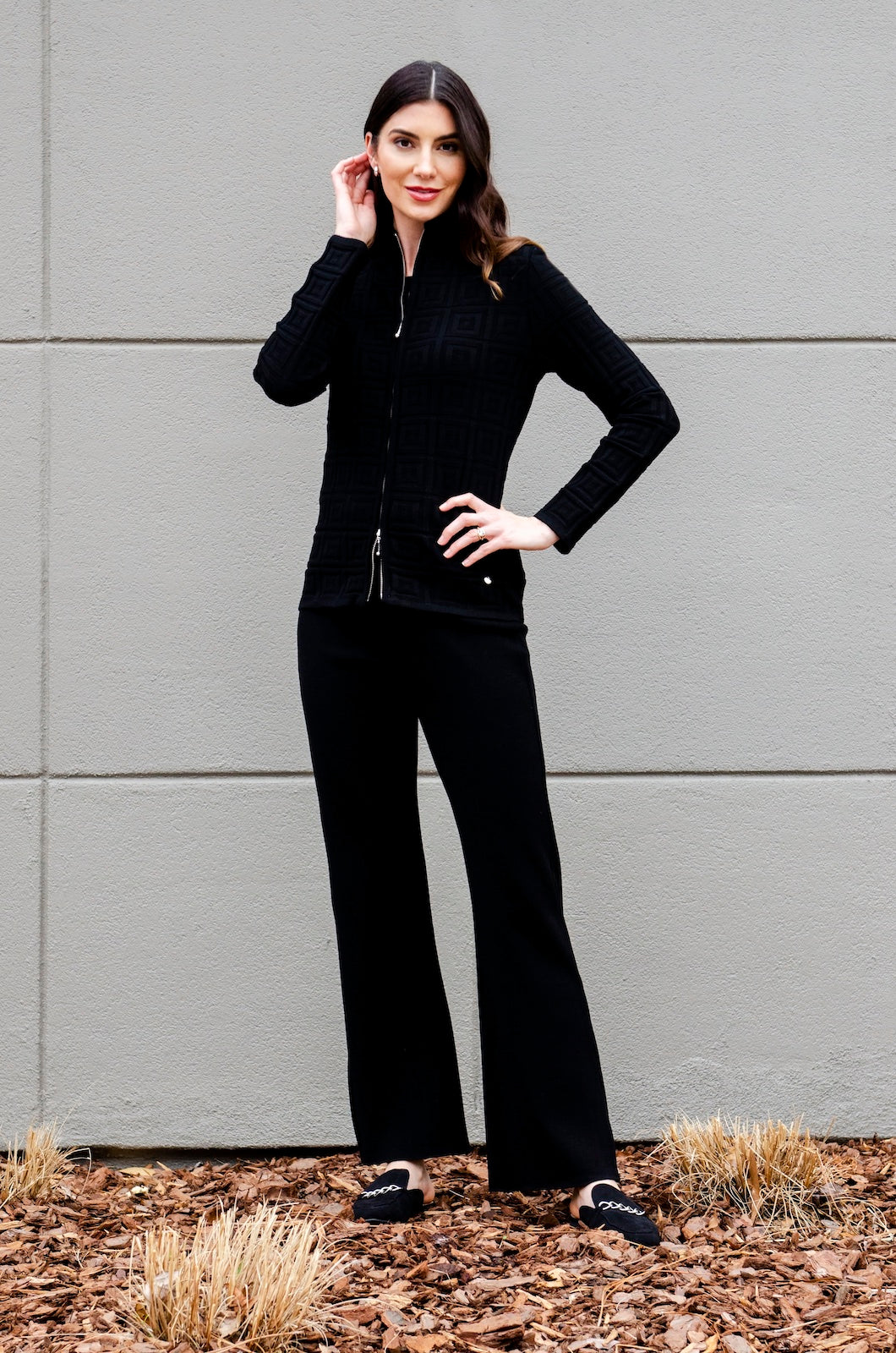 Woman wearing a black outfit standing against a gray wall.