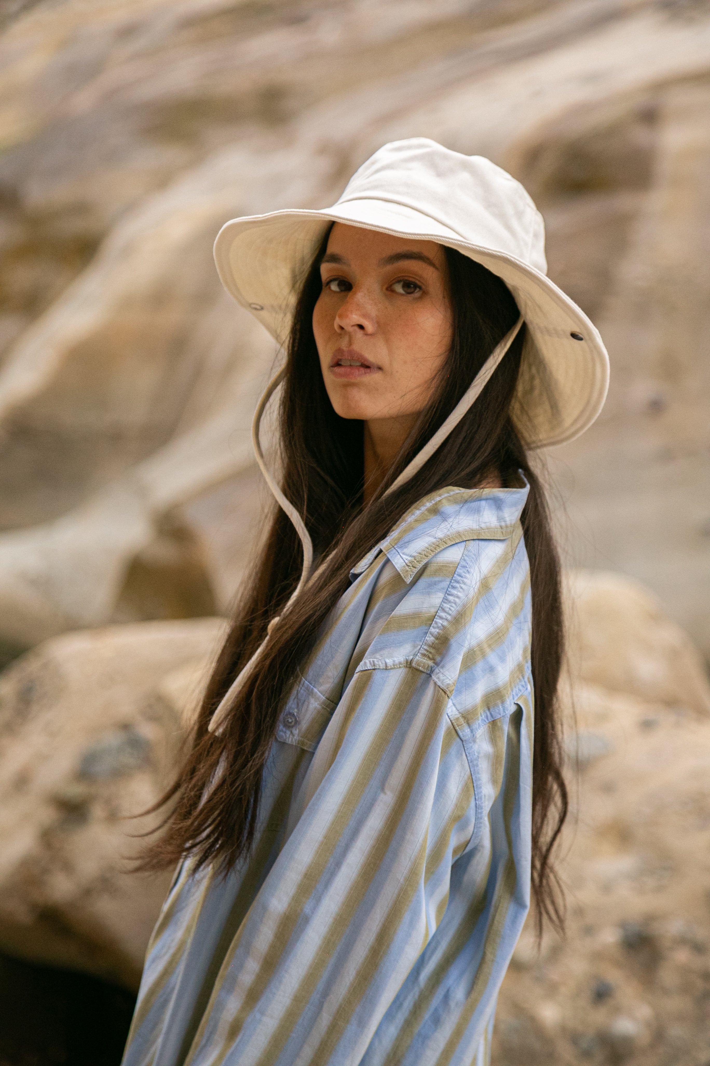 Woman wearing a white bucket hat and striped shirt in a natural setting