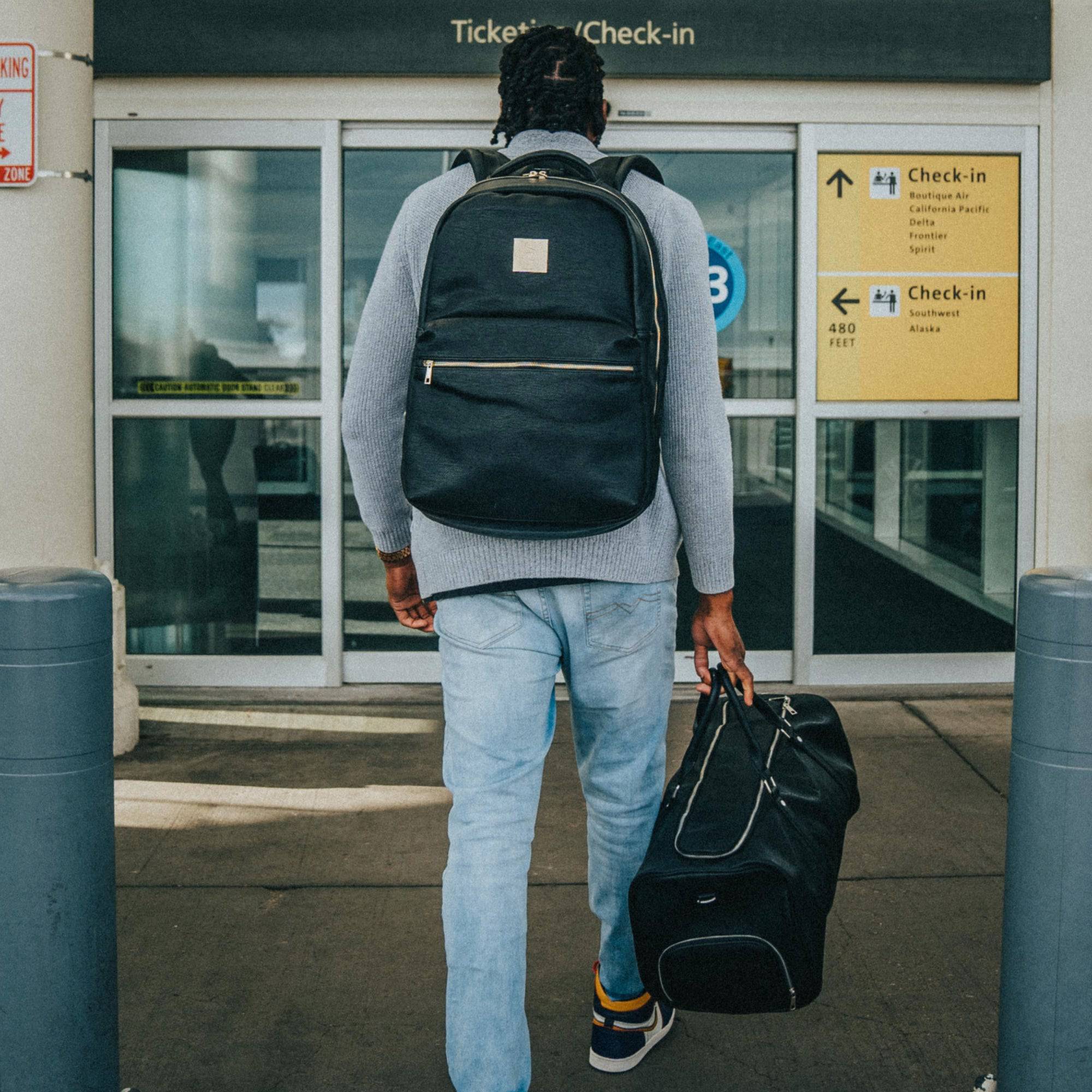 Man with a backpack and suitcase walking towards an airport check-in area