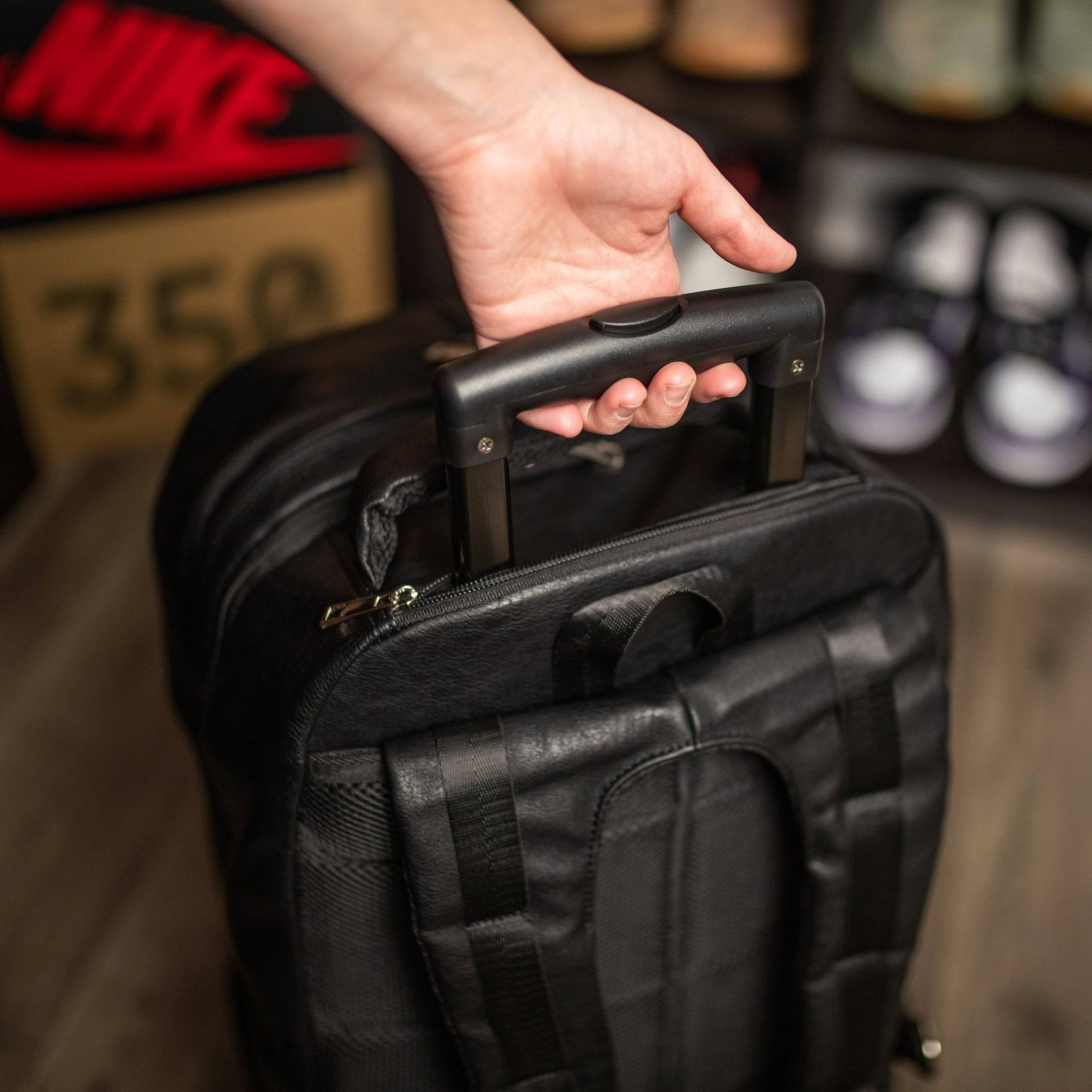 Person holding a black suitcase with a blurred background of shoes and a Nike sign.