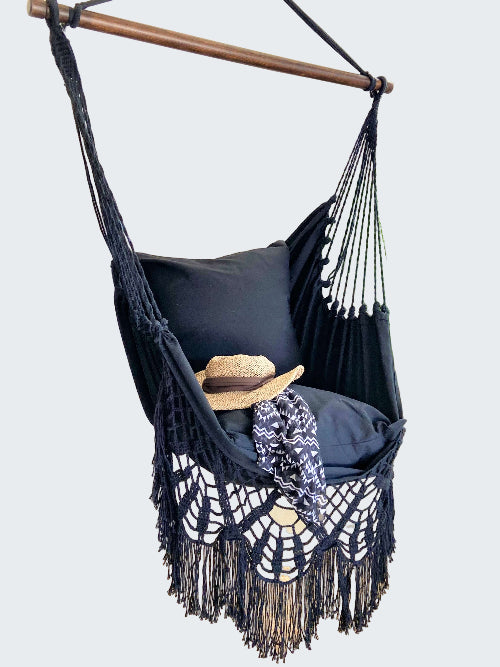 Black macrame hammock chair with pillows and a hat in a room setting.