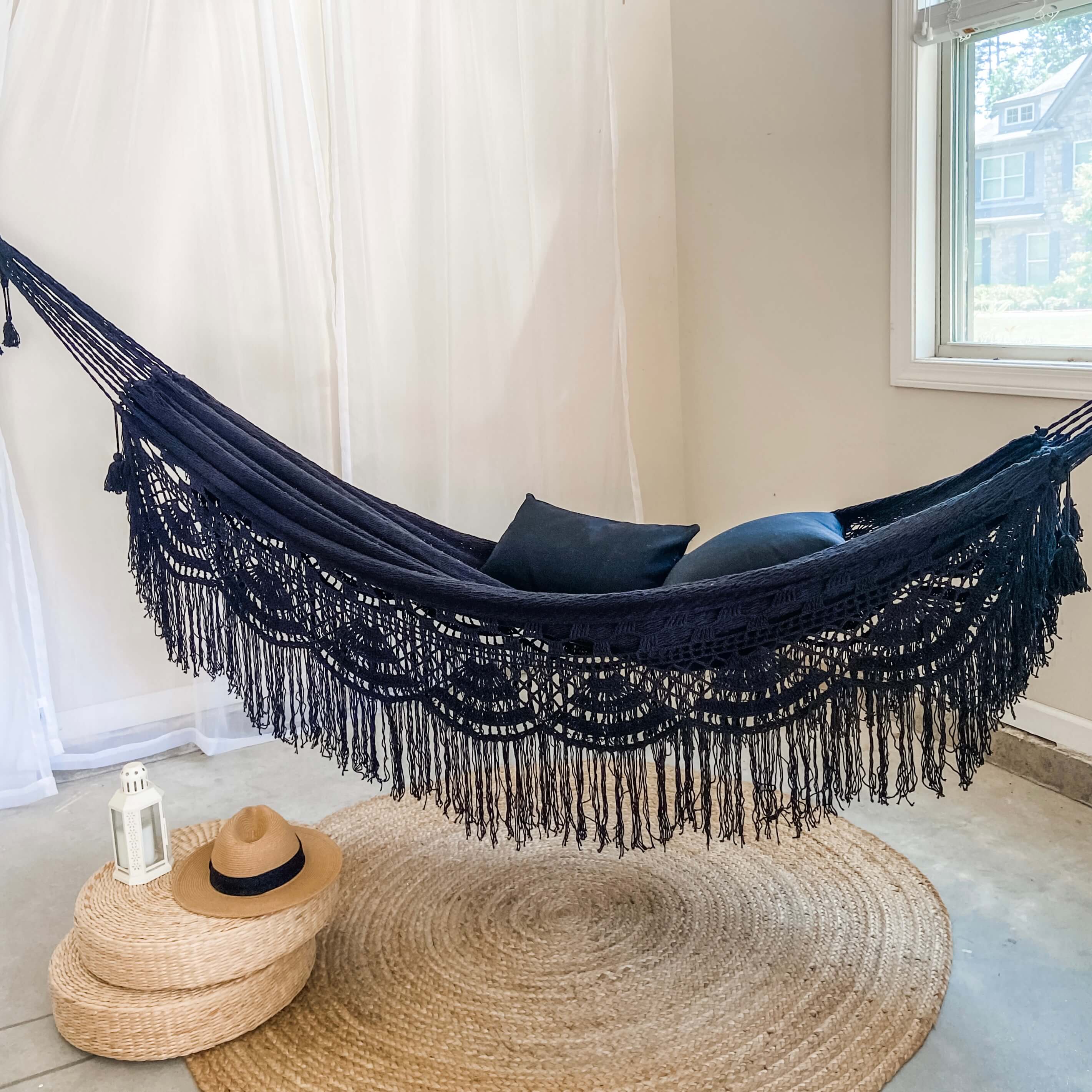 Navy blue hammock with tassels in a room with a window and rug.