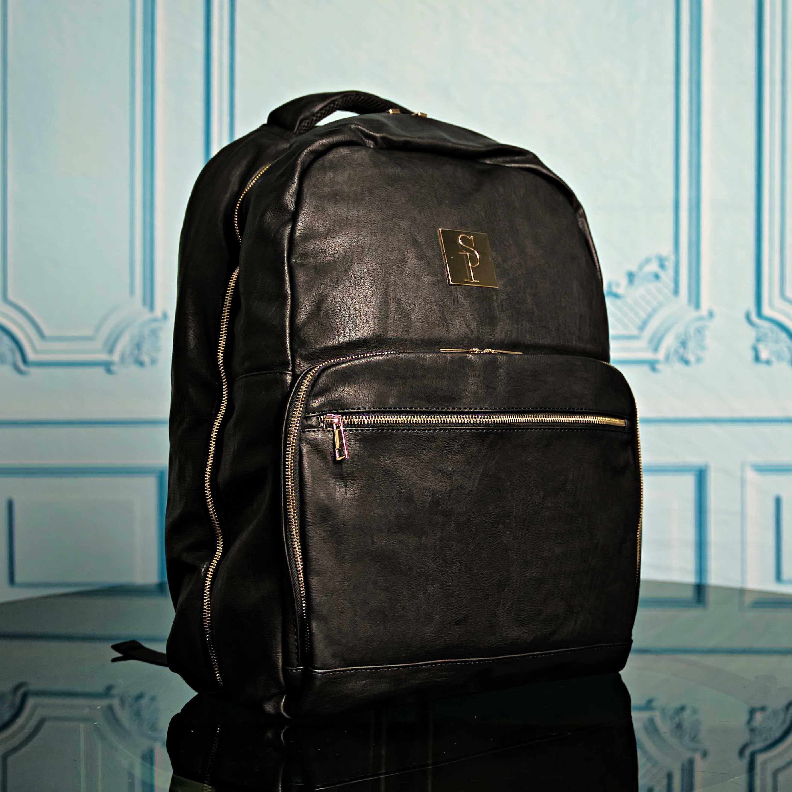 Black backpack with a logo on a reflective surface and light blue decorative wall background