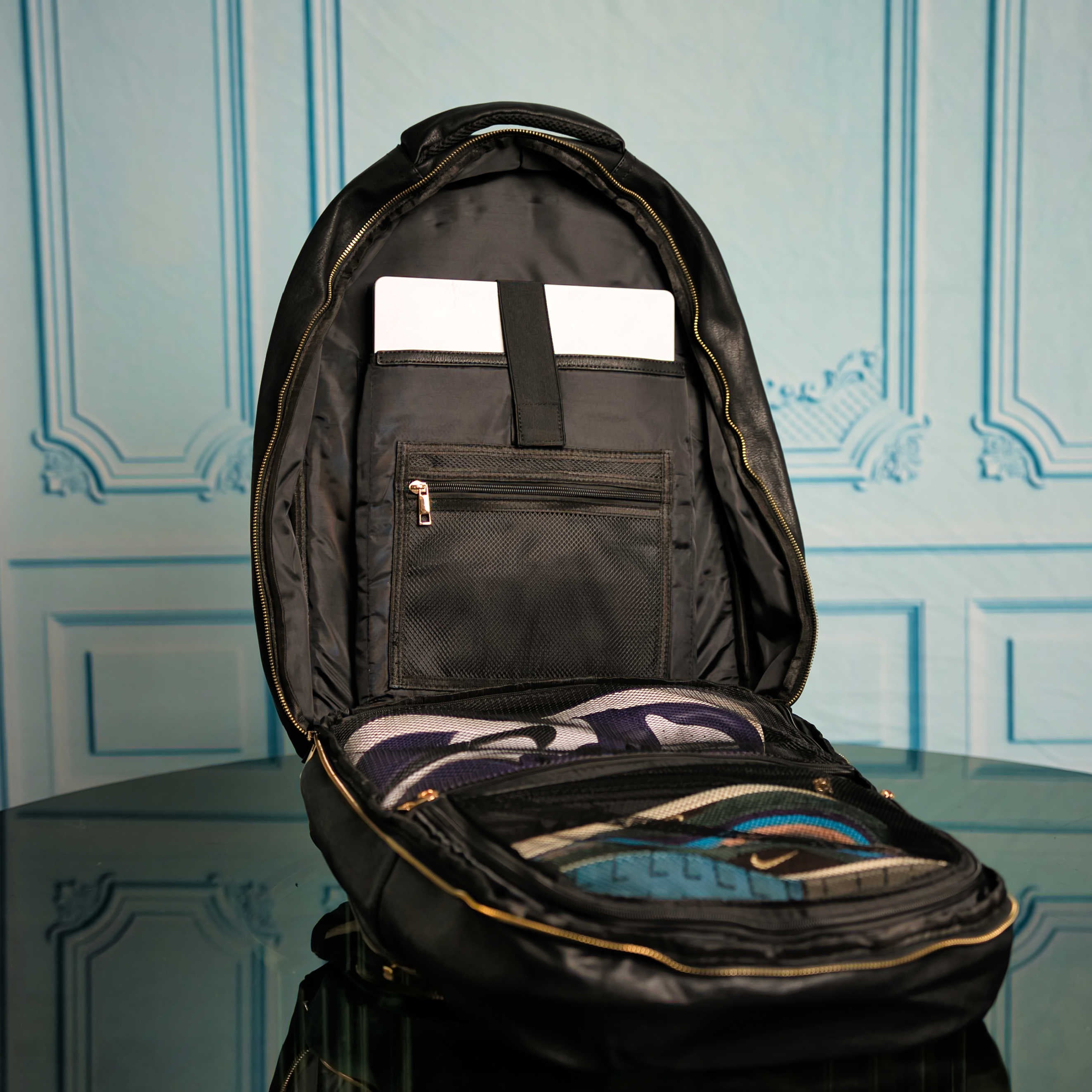 Black backpack with open front pocket against a decorative wall.