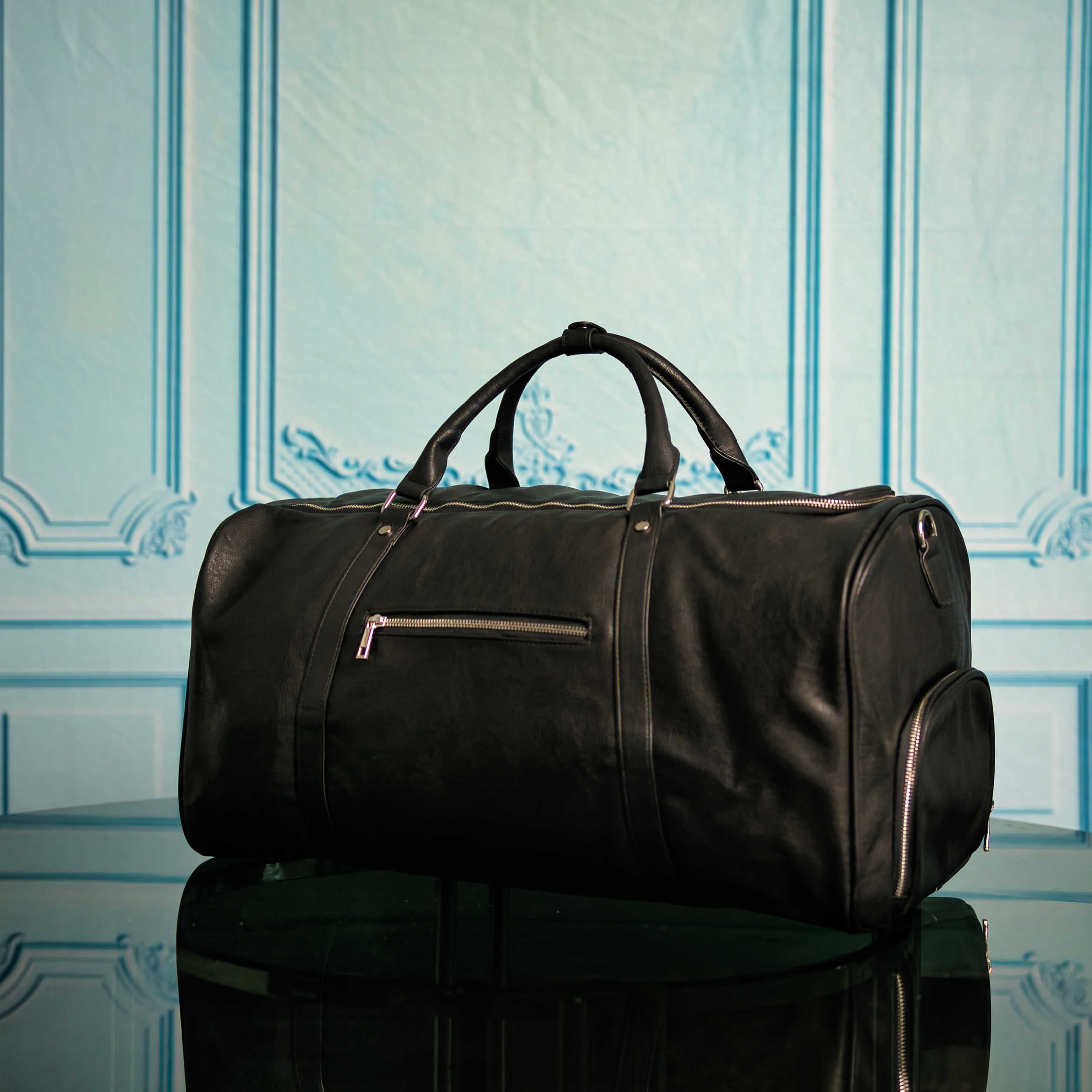 Black duffel bag on a reflective surface with a decorative blue wall in the background