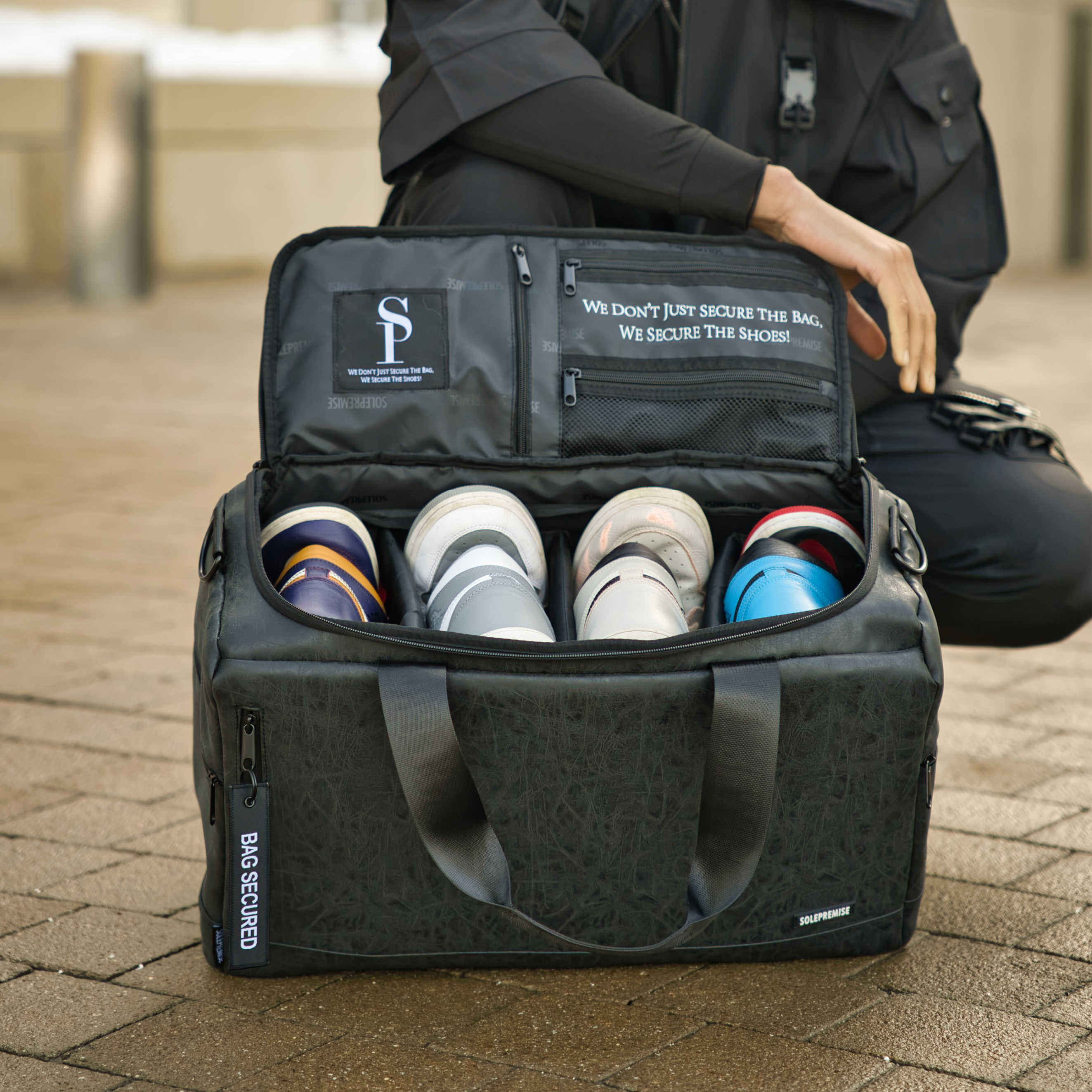 Black security bag with compartments for shoes, featuring a visible brand logo and text.