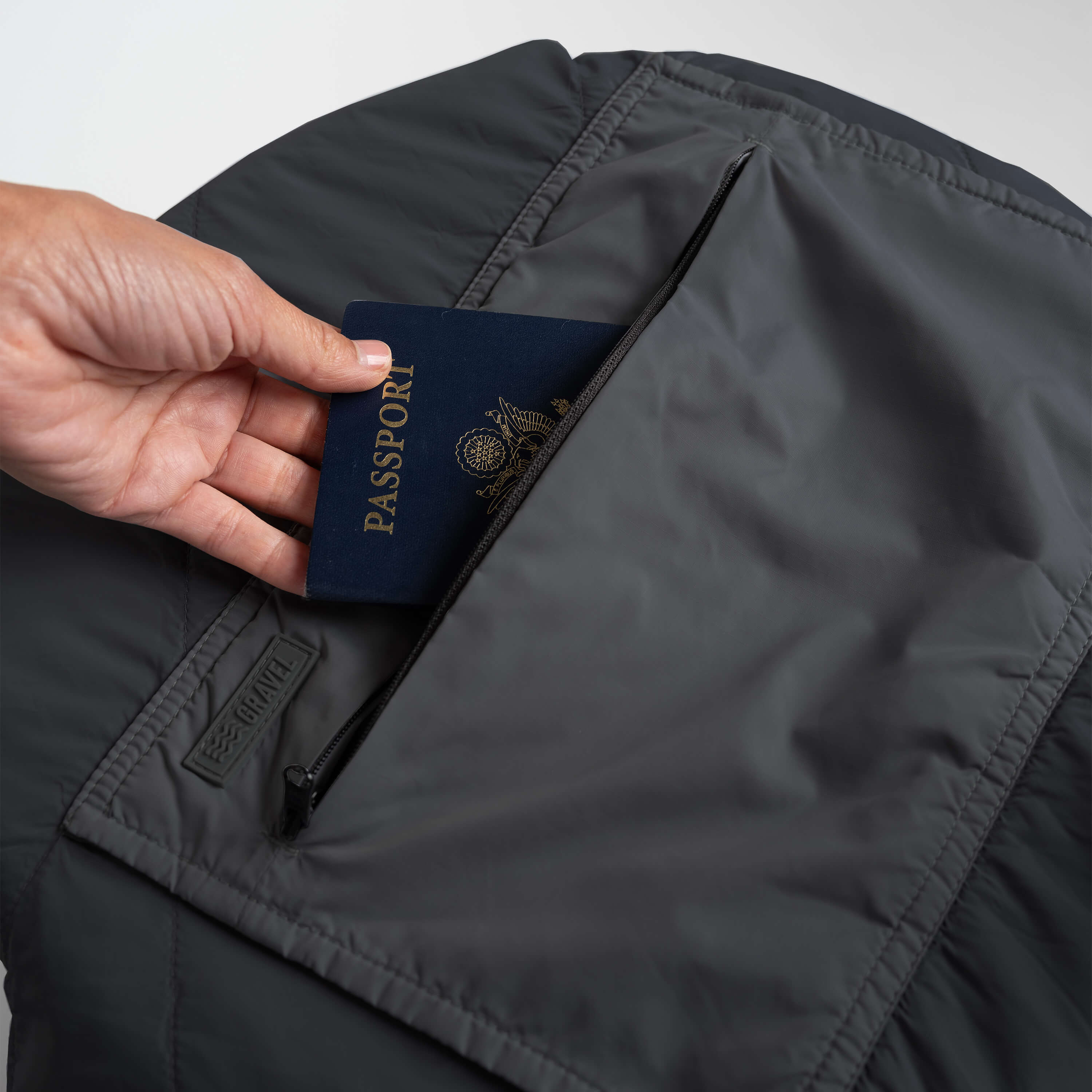 Hand placing a passport into a dark gray jacket pocket.