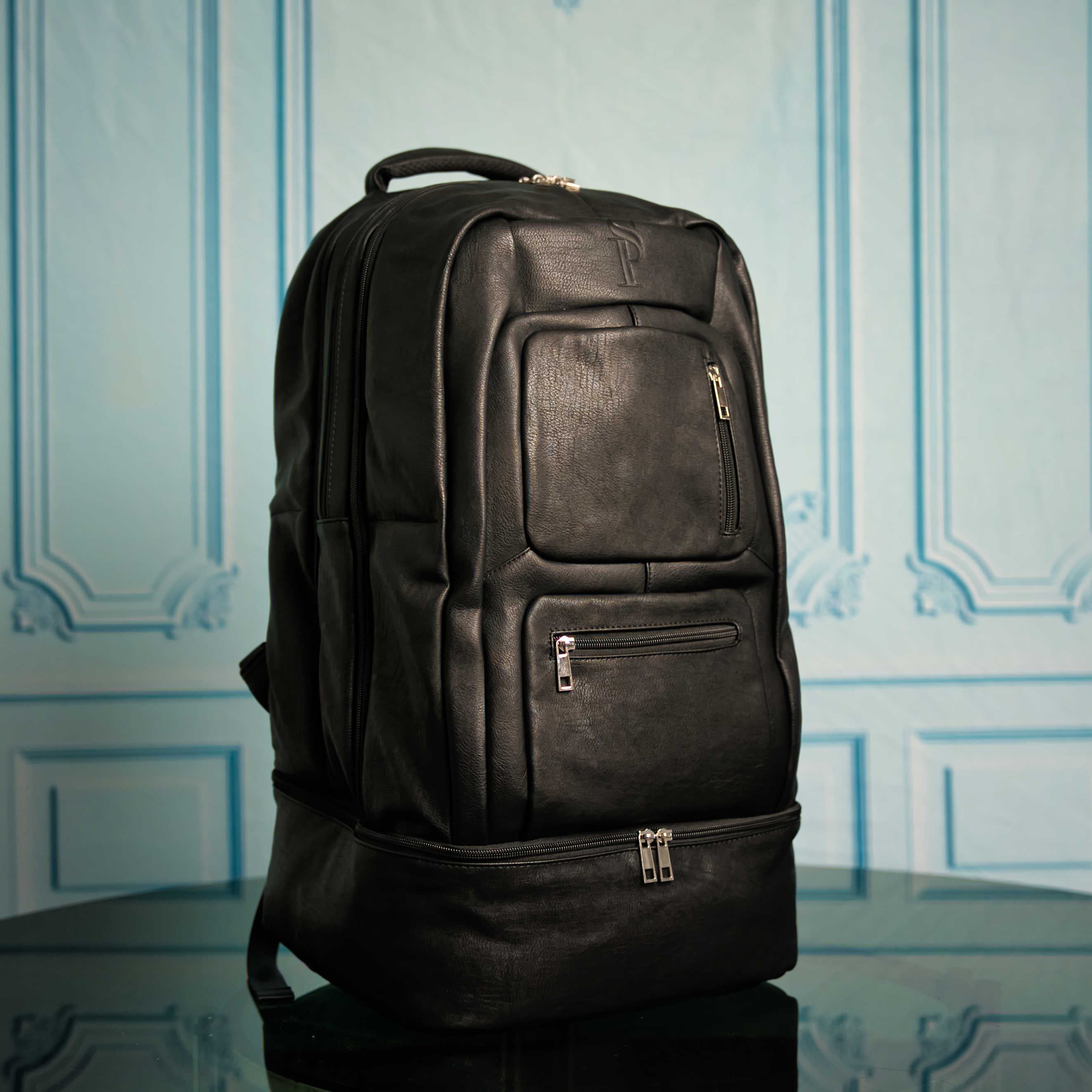 Black leather backpack on a reflective surface with decorative wall in the background