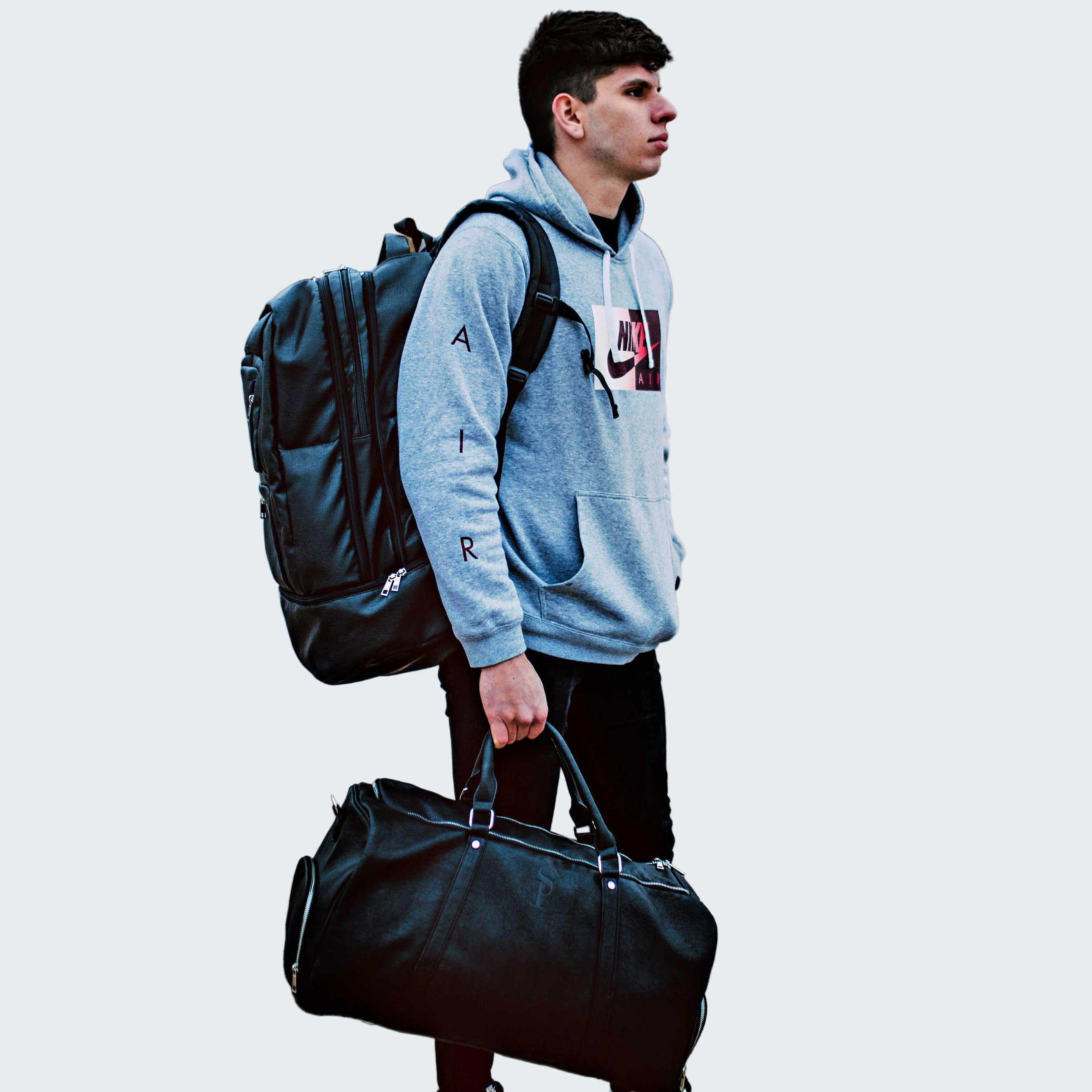 Person with a backpack and duffel bag standing on a sidewalk