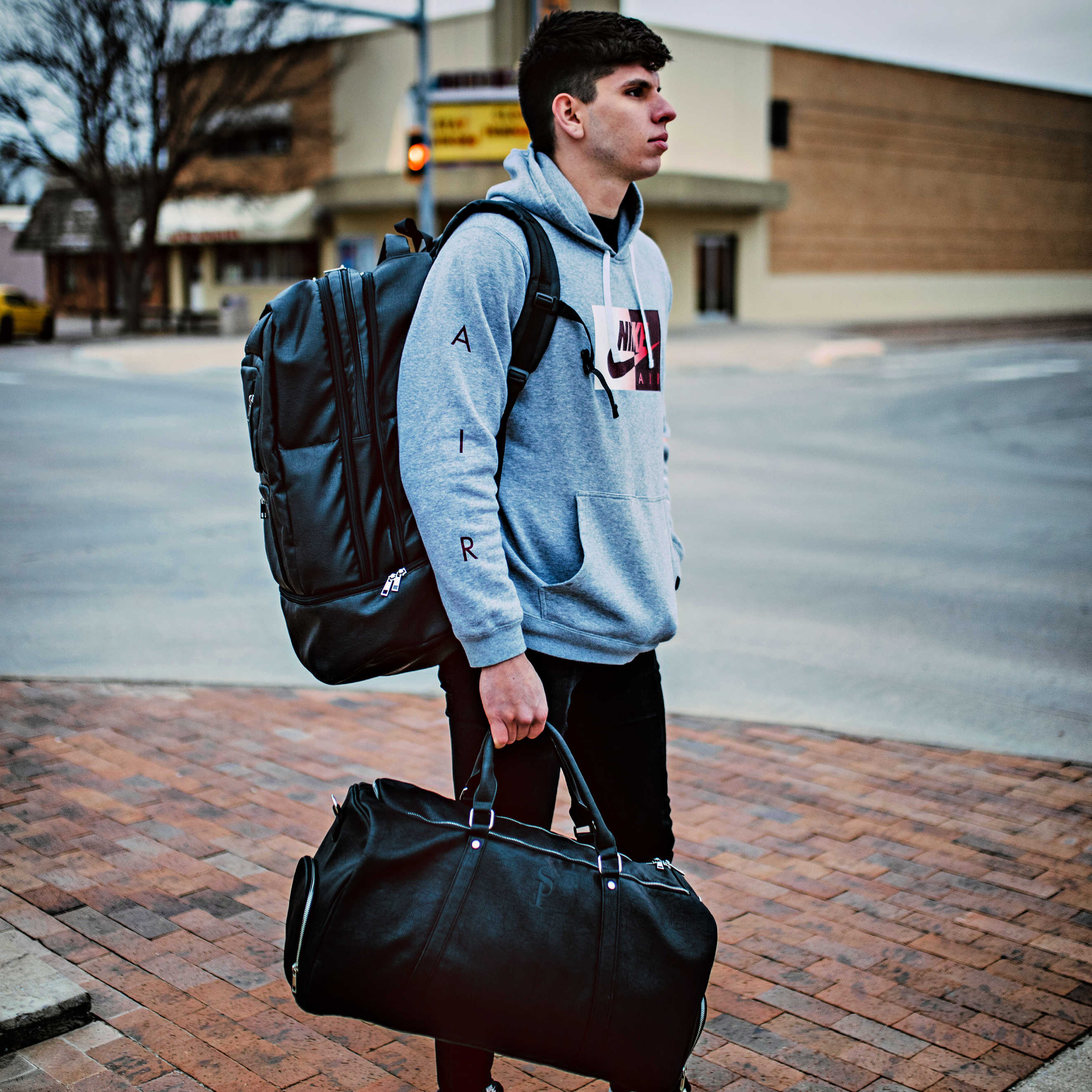 Person with a backpack and duffel bag standing on a sidewalk