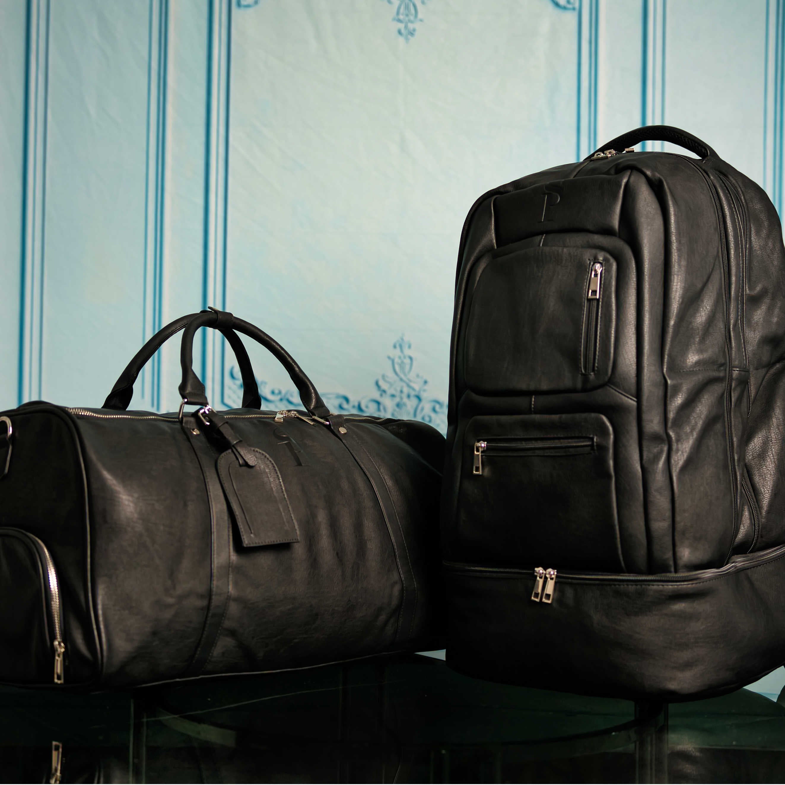 Two black leather bags, a duffel bag and a backpack, on a reflective surface with a light blue striped background.
