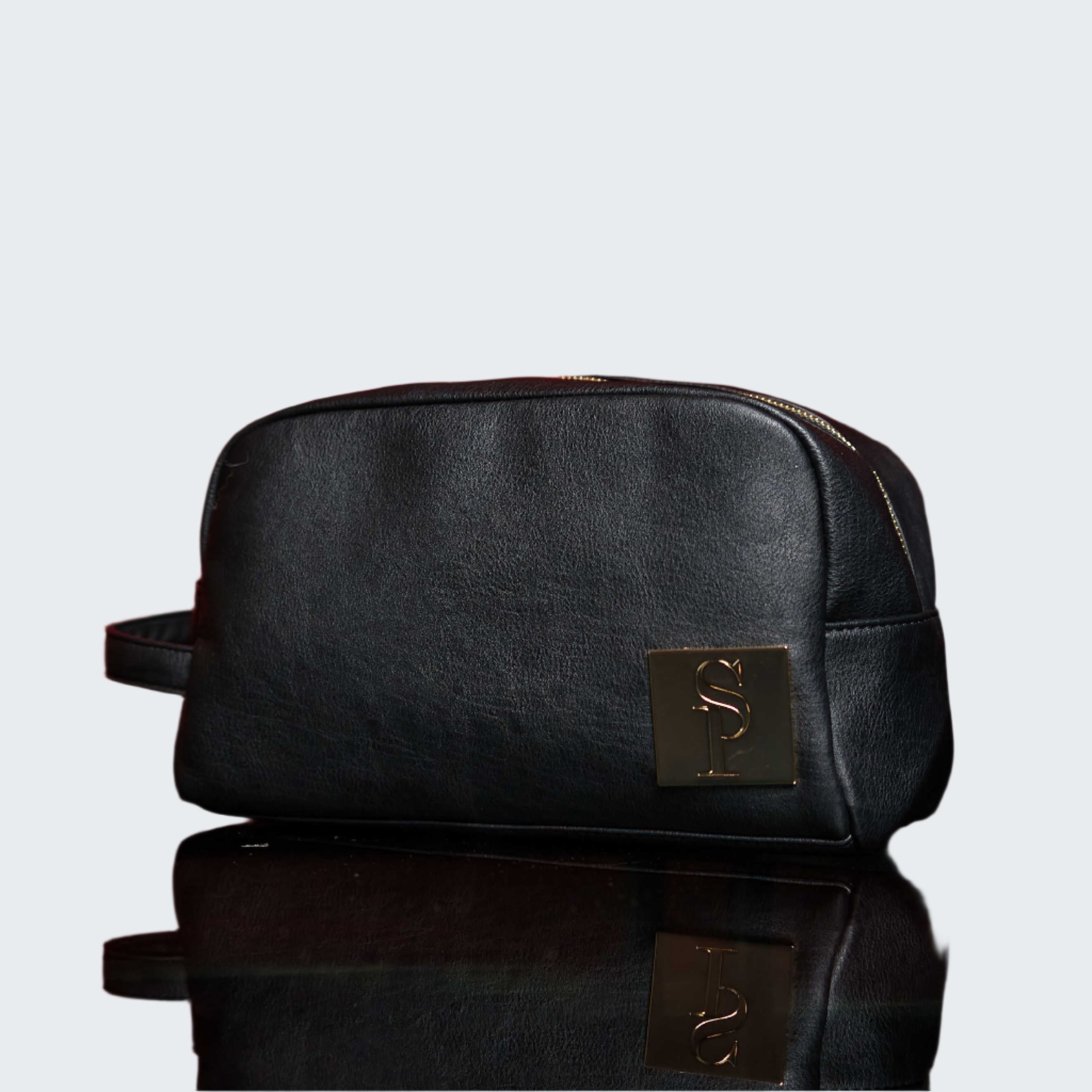 Black toiletry bag with gold clasp on a reflective surface against a red background