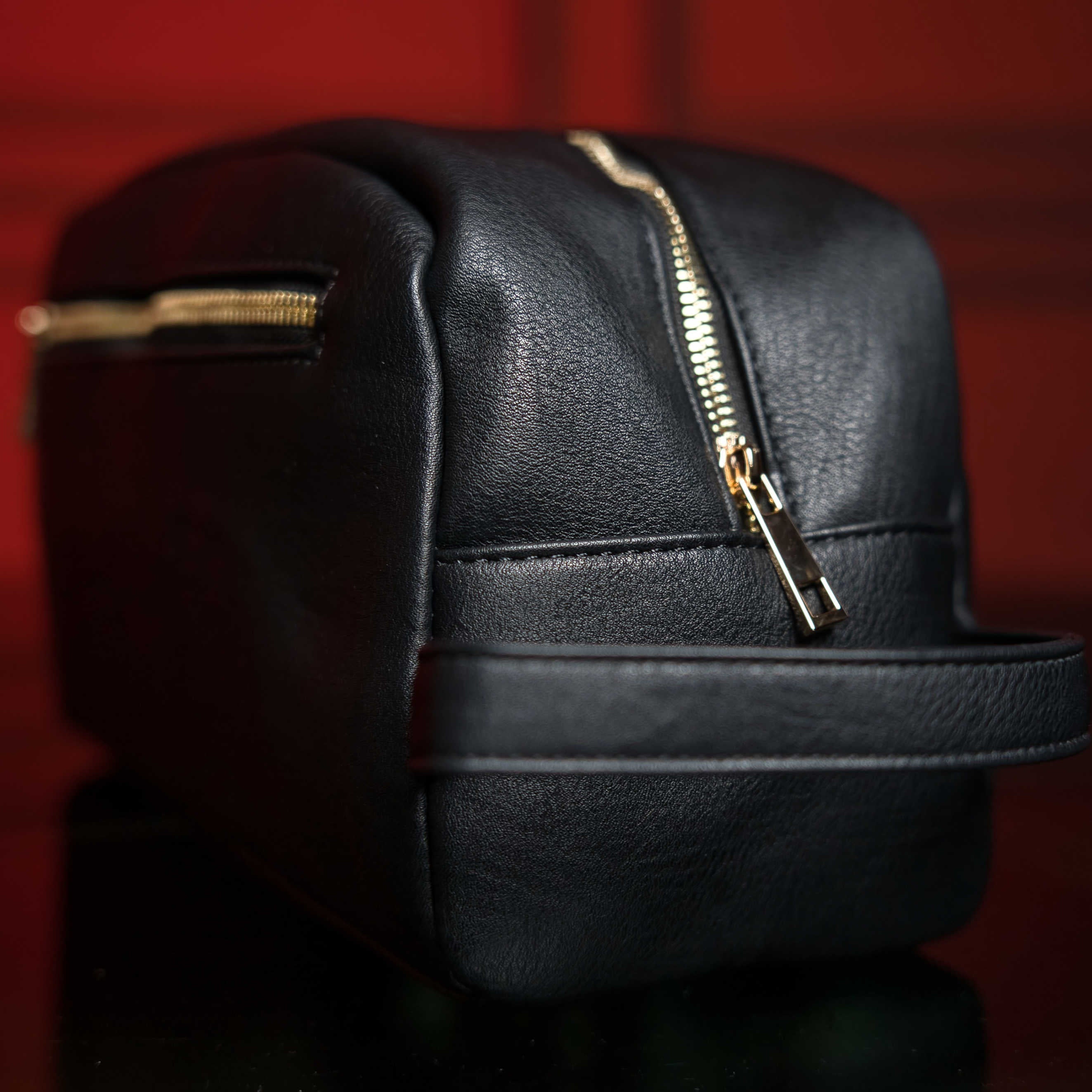 Black leather bag with gold zipper on a dark red background