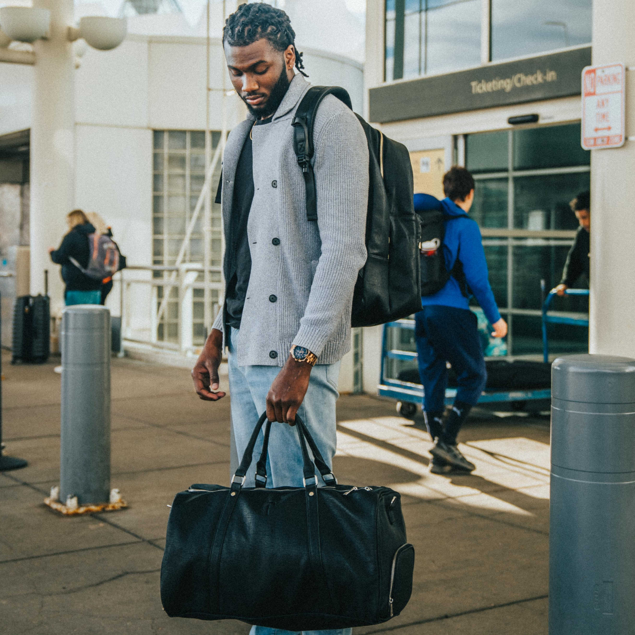 Man with a black duffel bag and backpack walking through an airport terminal.
