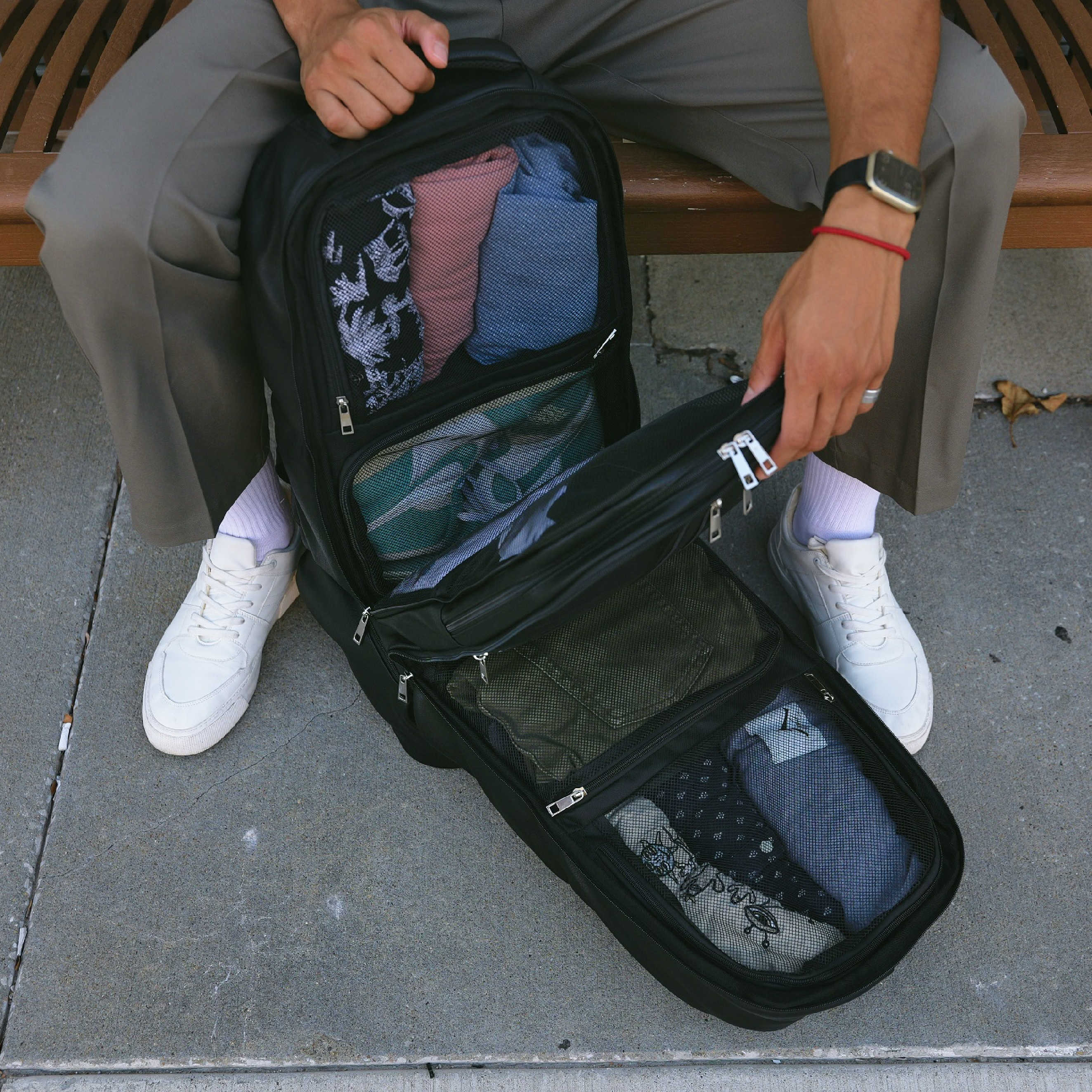 Person packing clothes into a black suitcase on a bench.