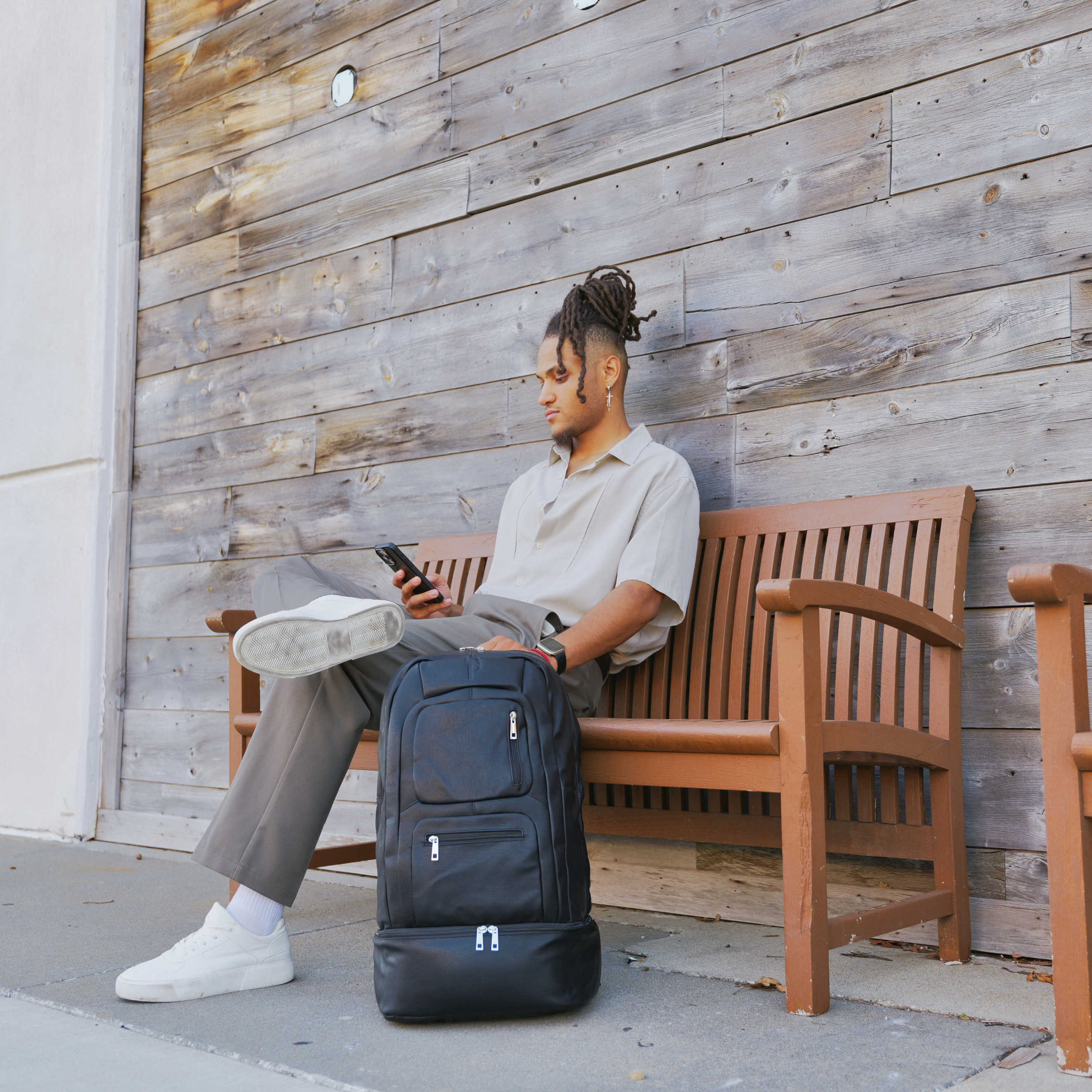 Man sitting on a bench with a suitcase and tablet, against a wooden wall.