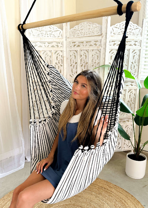Woman sitting in a black and white striped hammock in a bright room with plants.