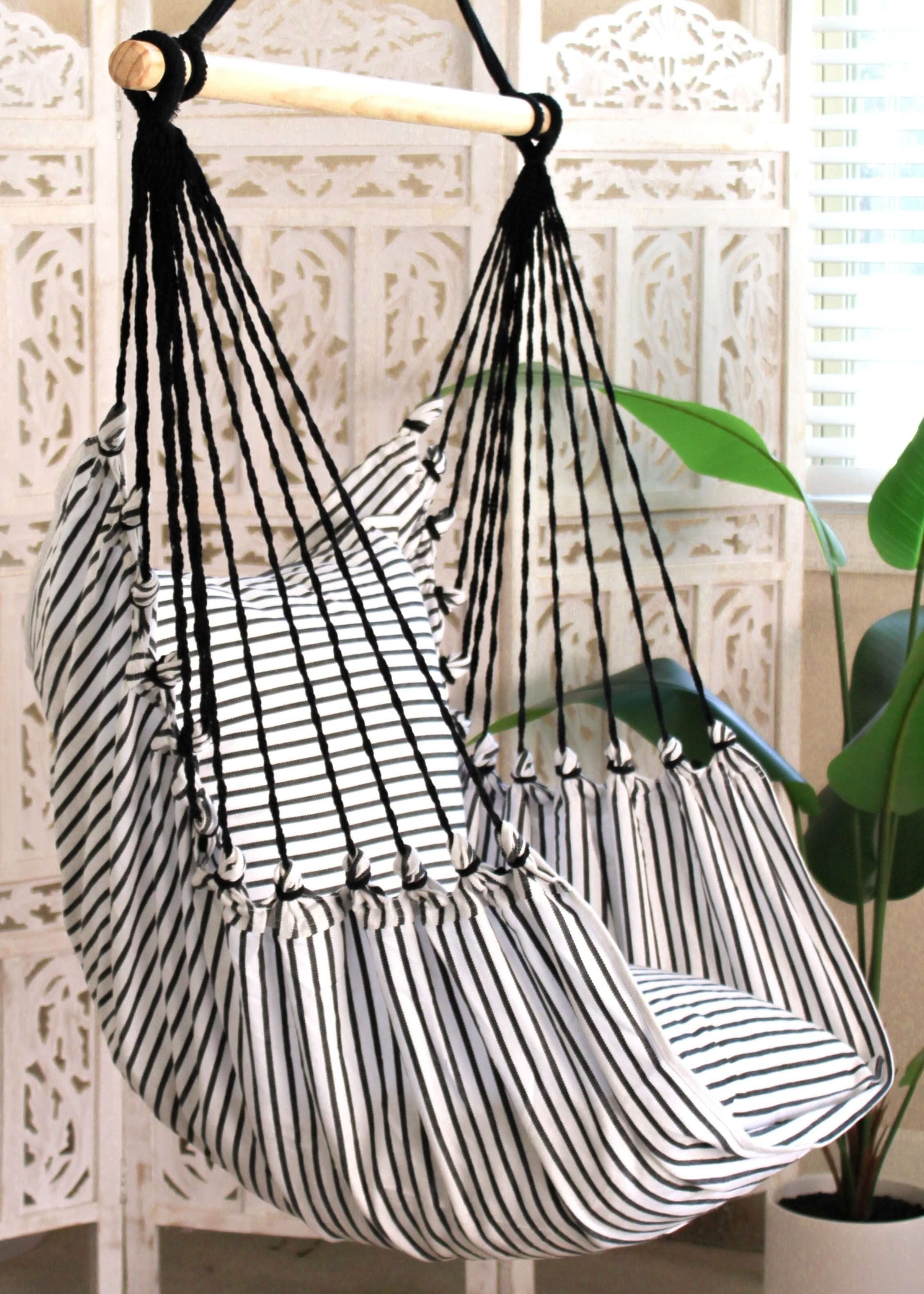 Black and white striped hammock chair hanging against a decorative wall with plants.