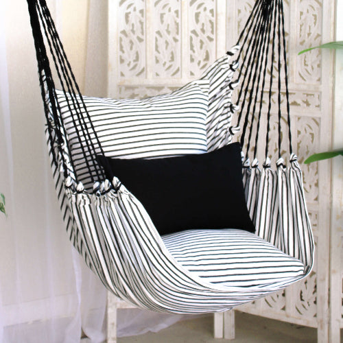 Black and white striped hammock chair with a black pillow against a white lattice background