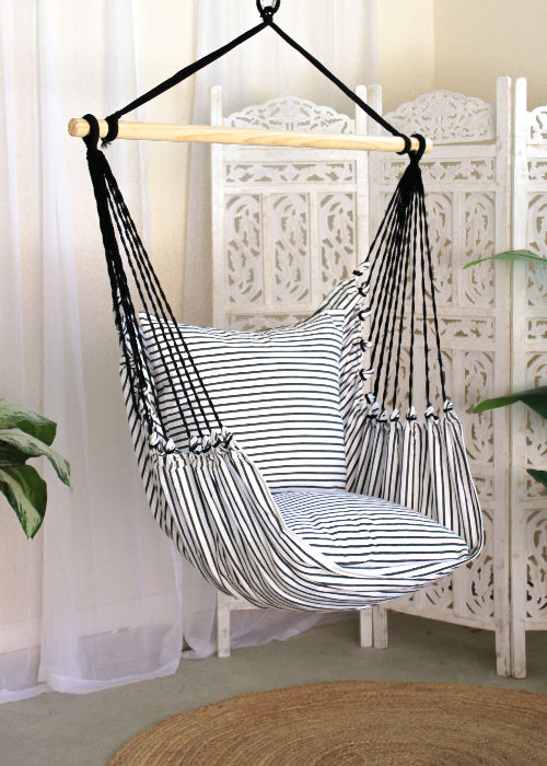 Striped hammock chair hanging against a white curtain and decorative screen.