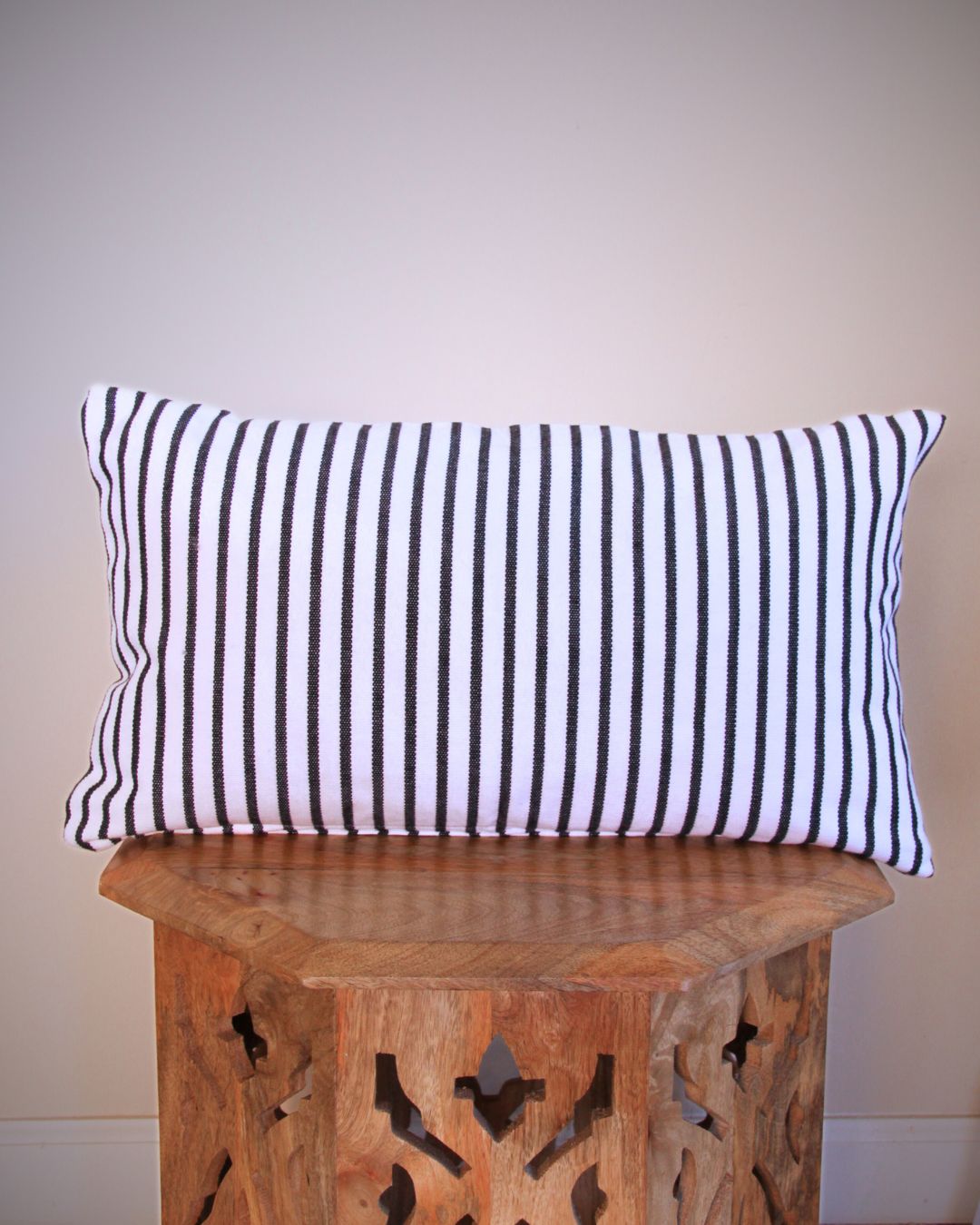 Striped pillow on a wooden stool against a plain wall