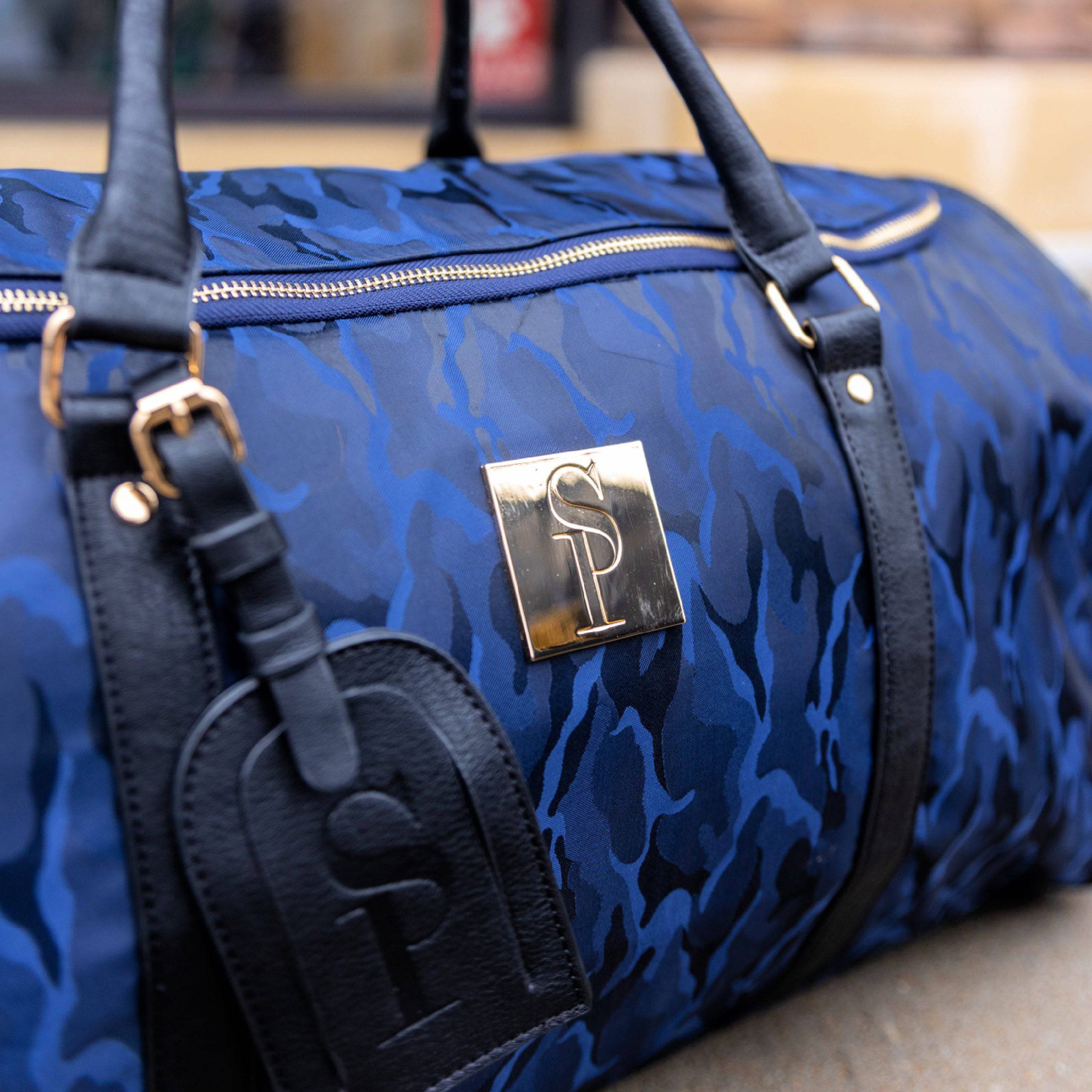 Blue camouflage duffel bag with black straps and a logo on a blurred background