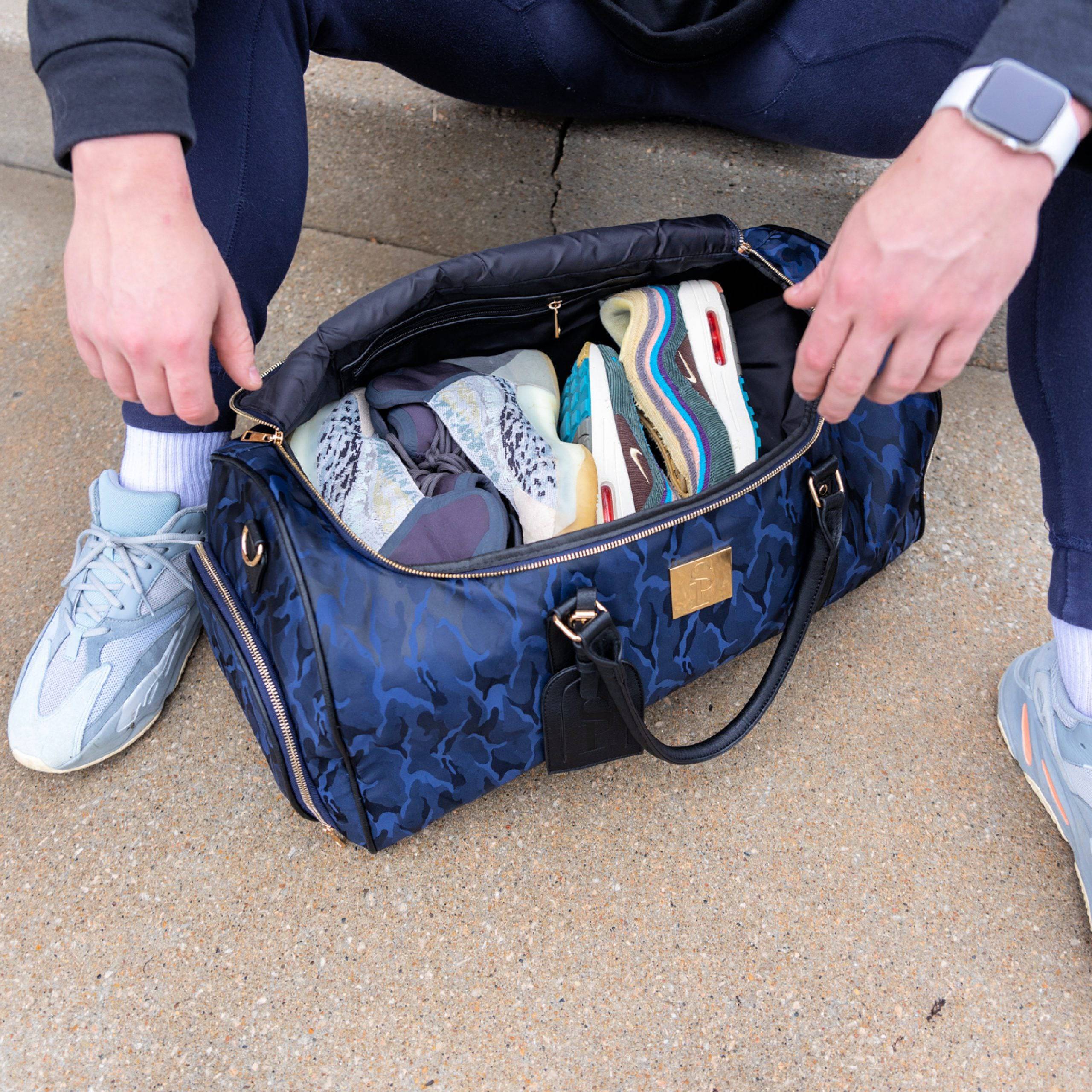 Person opening a blue duffel bag filled with various shoes on a concrete surface.