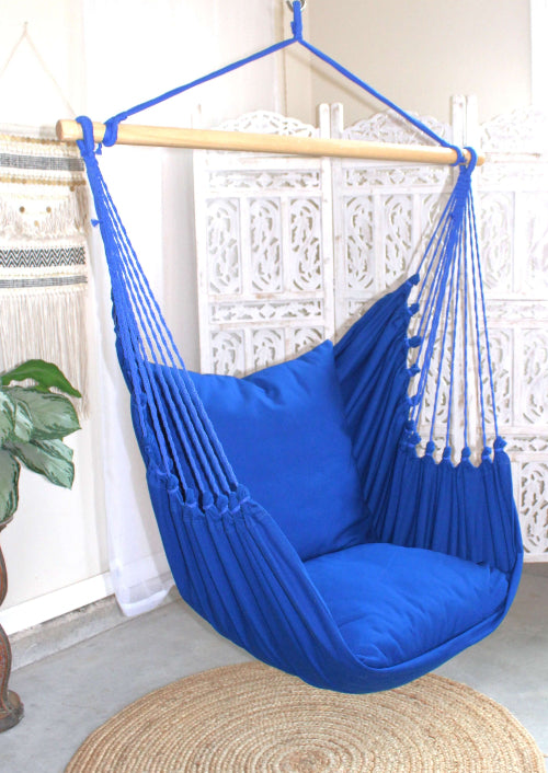 Blue hammock chair hanging from a wooden rod against a white wall.