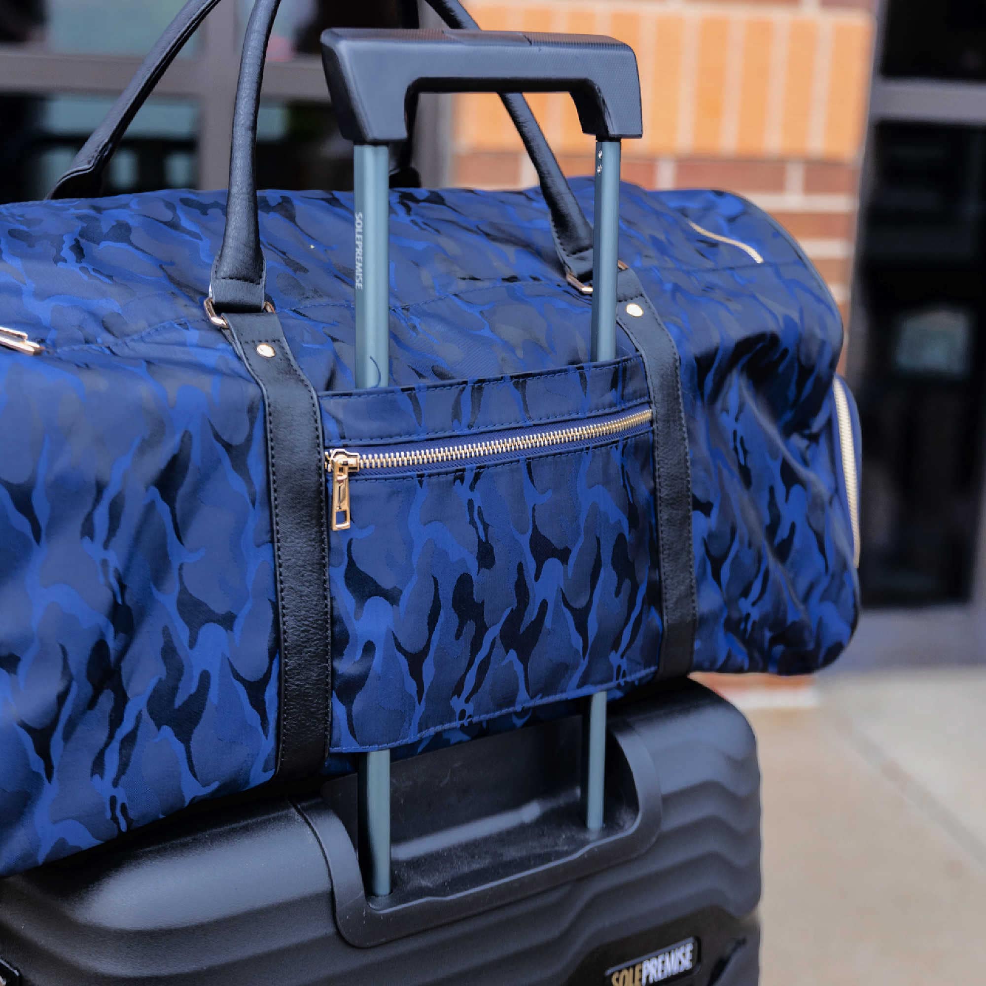 Blue camouflage-patterned duffel bag on top of a black suitcase with 'Self-Defense' branding.